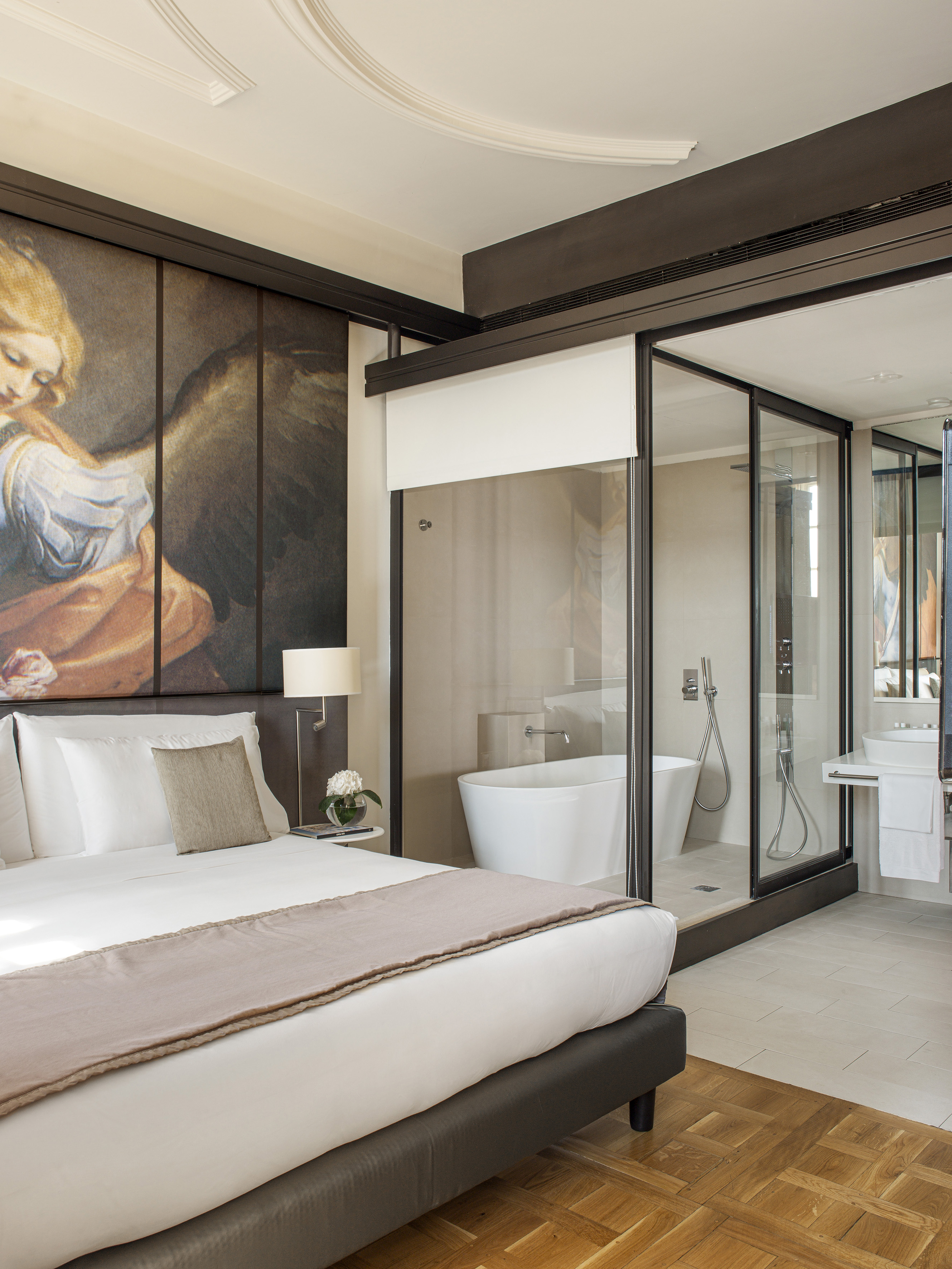 Luxury hotel bedroom with large art, and glass bathroom featuring modern tub.