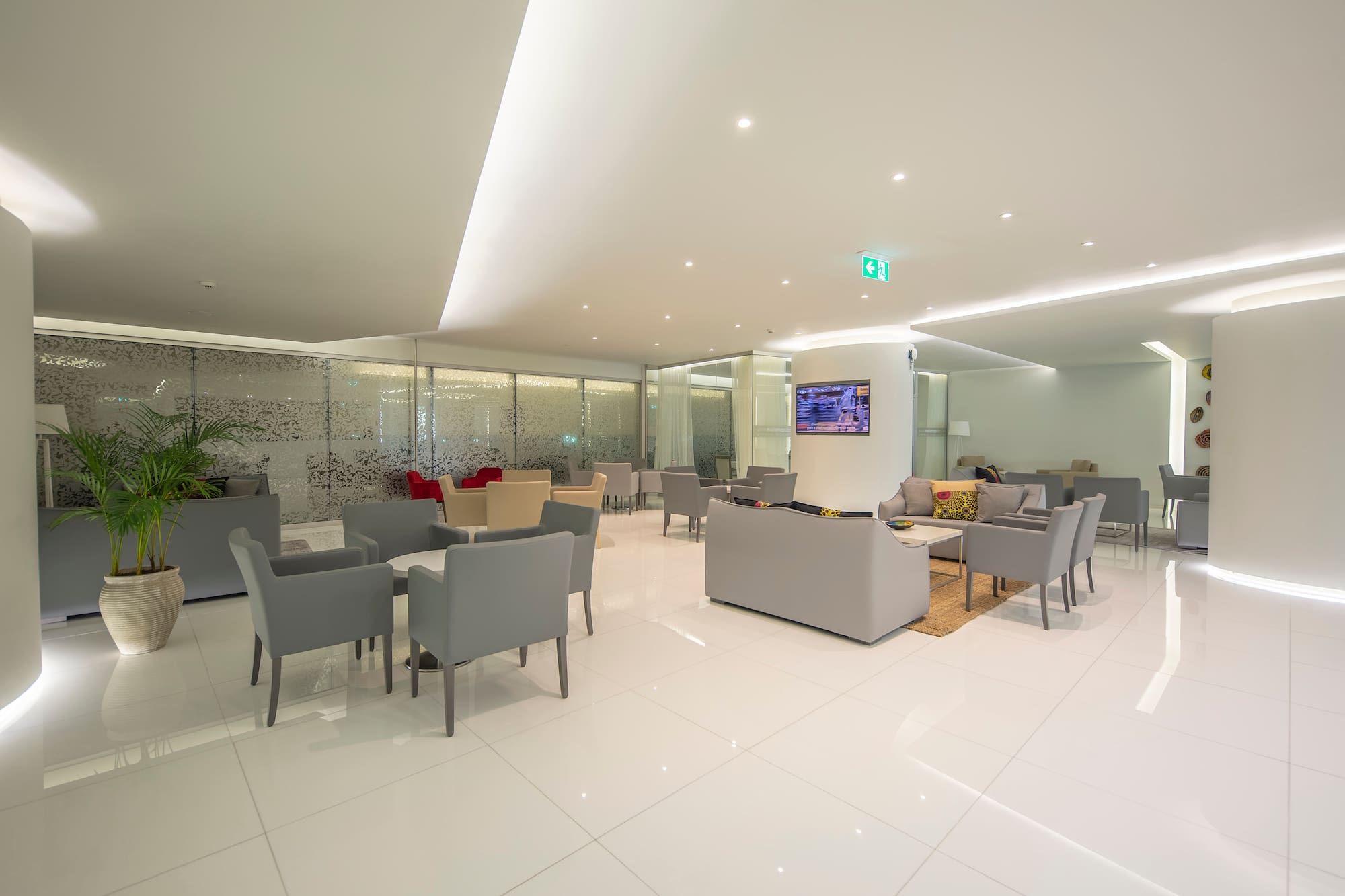 Bright modern lounge with gray seating, white tiled floor, and frosted glass.