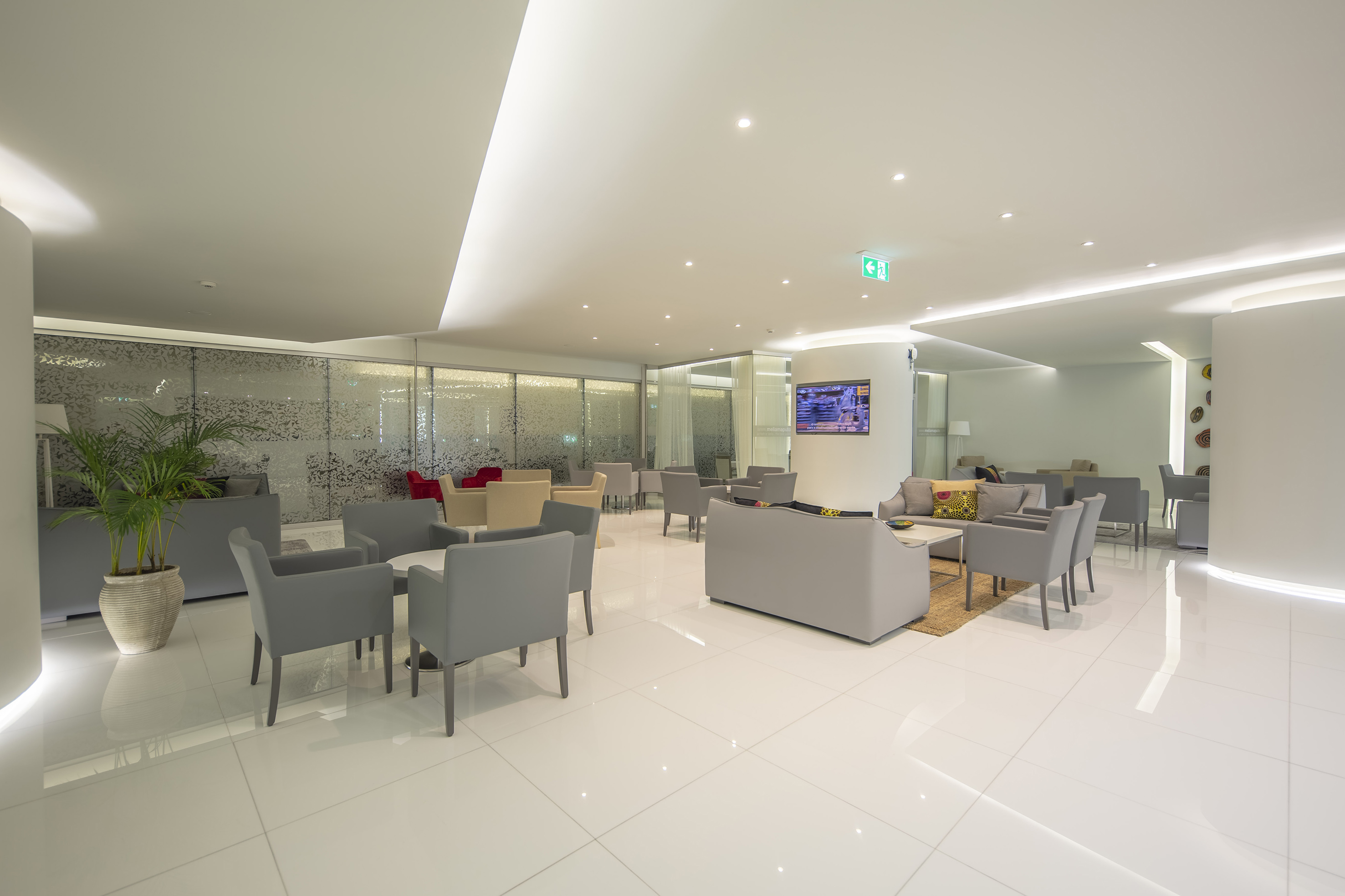 Bright modern lounge with gray seating, white tiled floor, and frosted glass.
