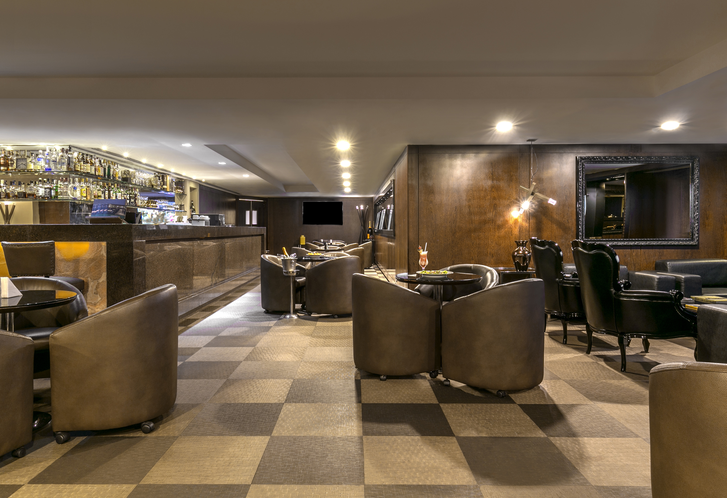 Hotel lounge bar with brown armchairs, full liquor bar, and checkered floor.
