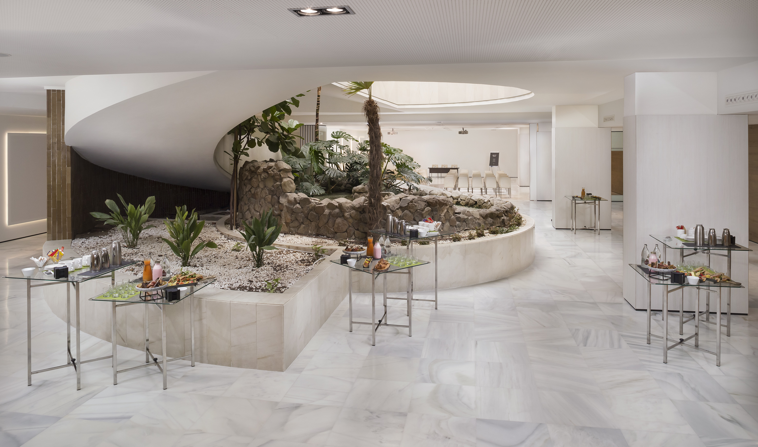 Modern hotel interior with indoor garden, buffet tables, and event space.