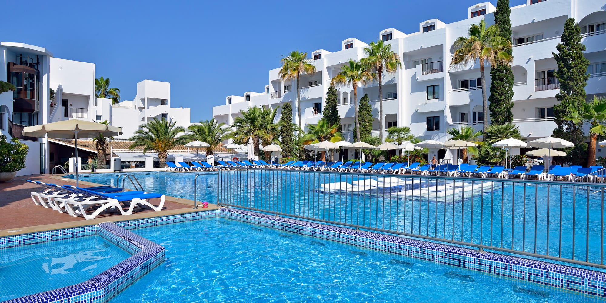 a pool with lounge chairs and a fence in front of a white building