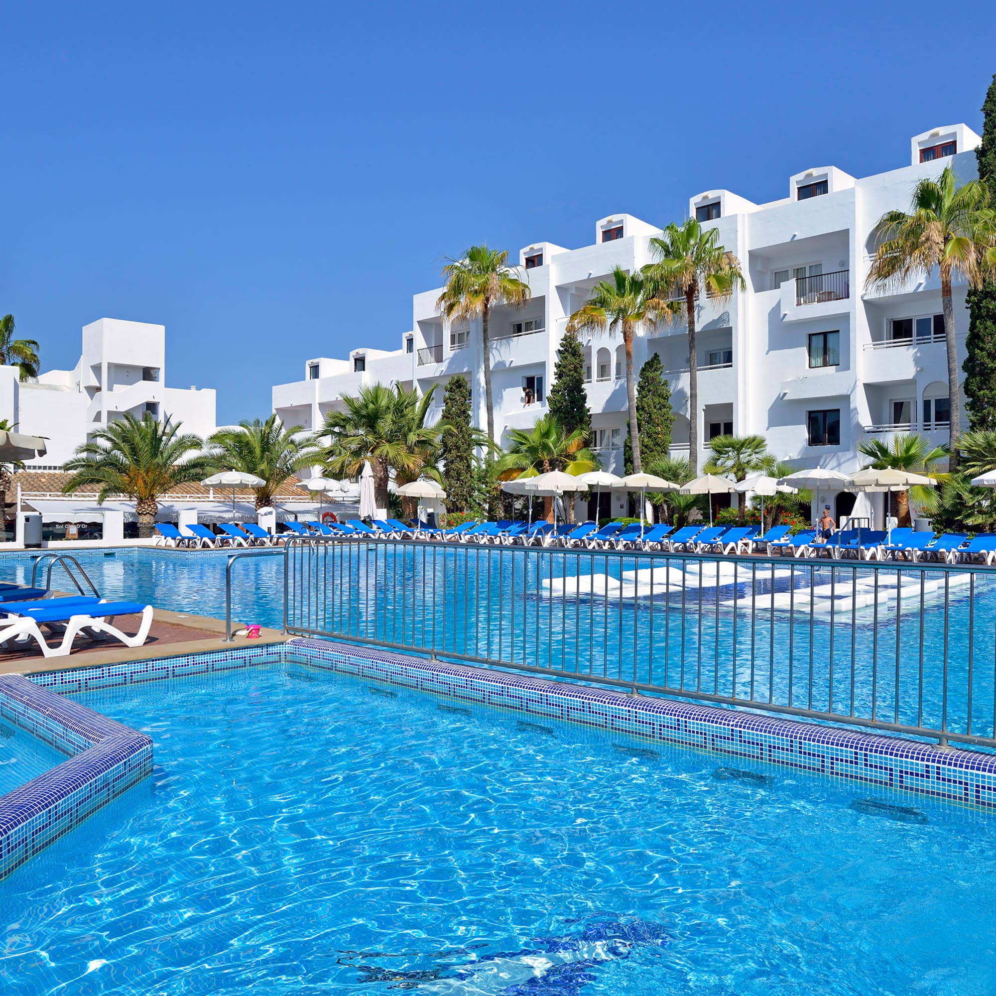 a pool with lounge chairs and a fence in front of a white building