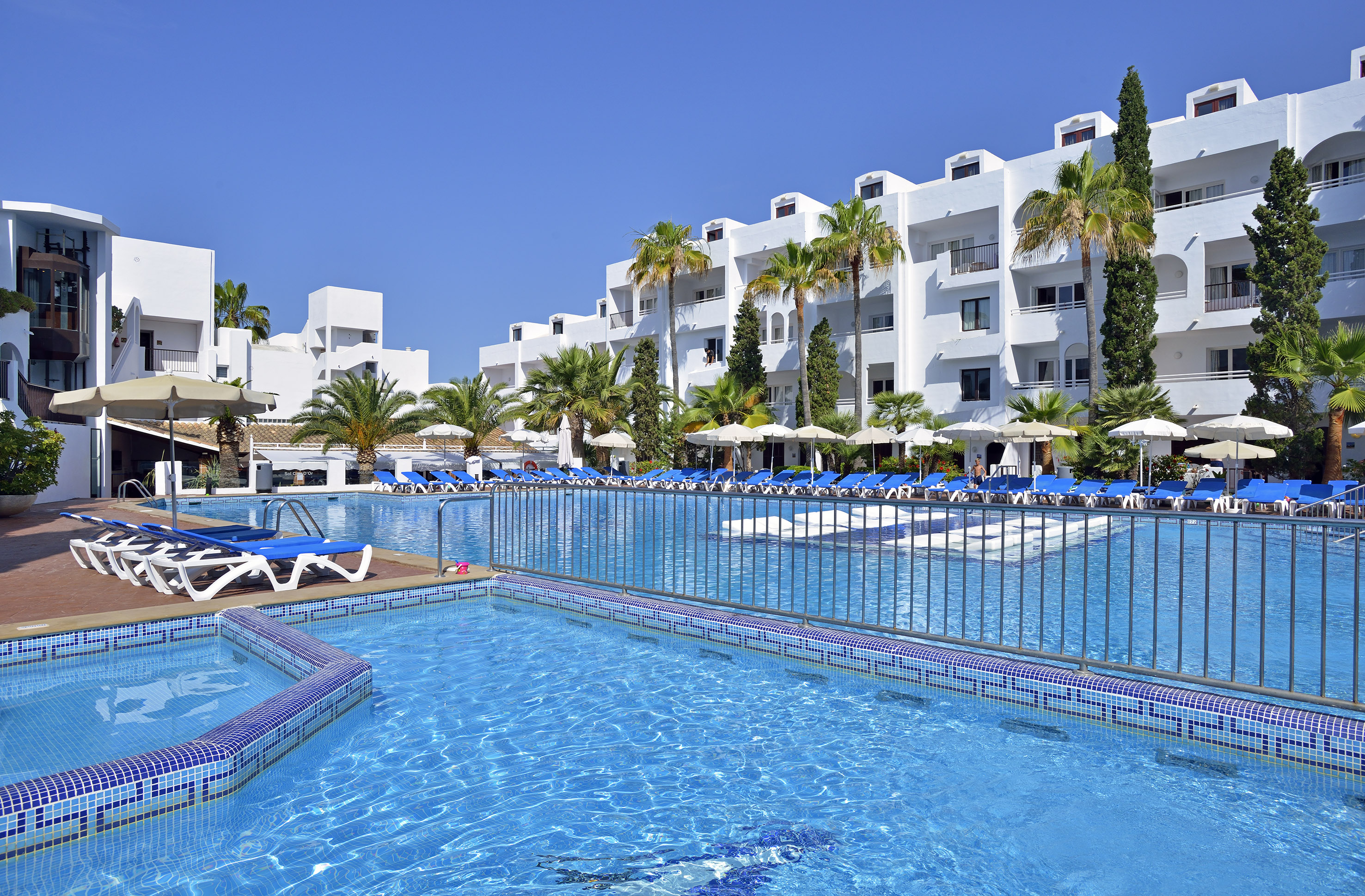 a pool with lounge chairs and a fence in front of a white building