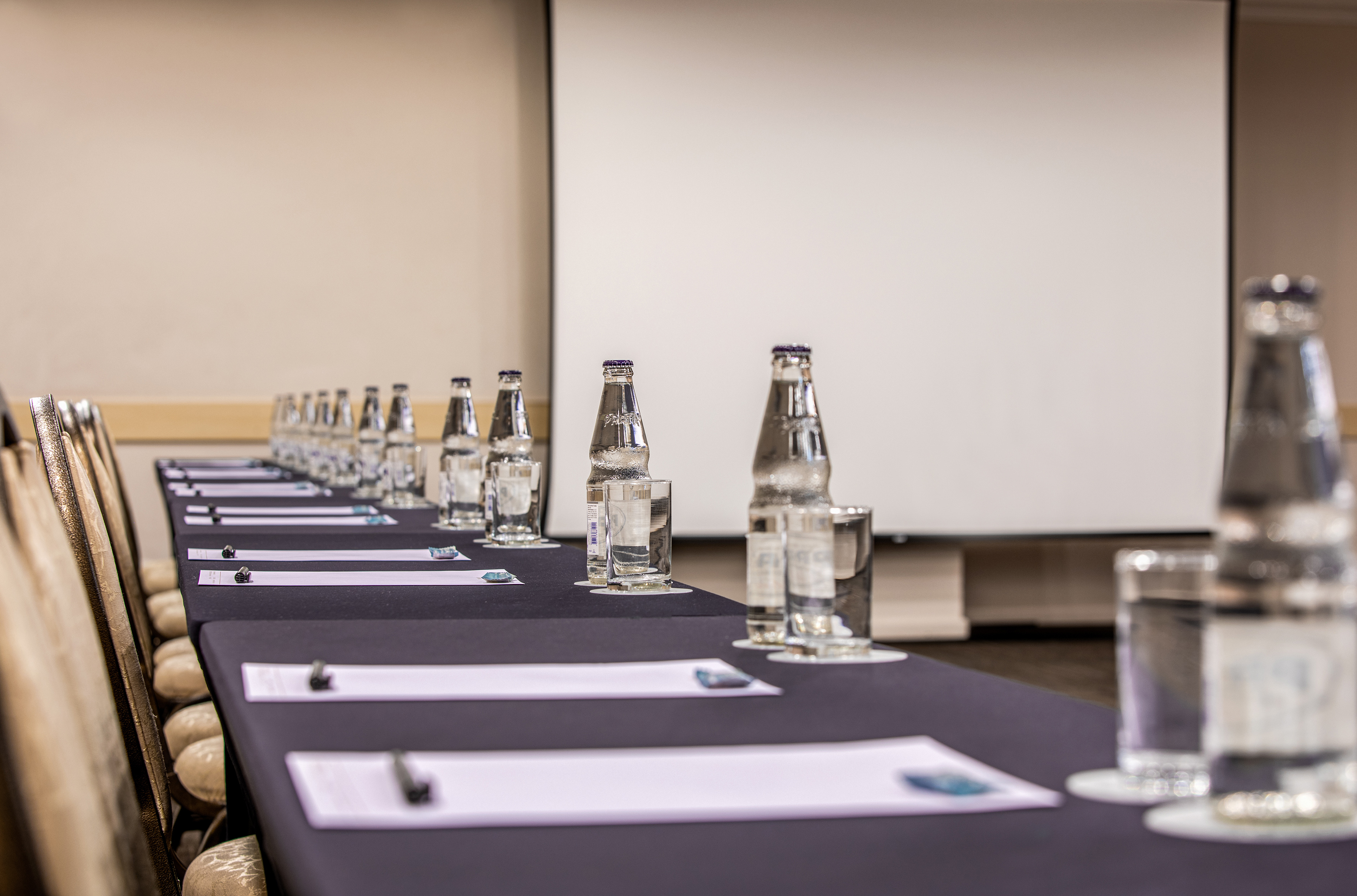Meeting room setup: tables with water bottles, notepads, and projector screen.