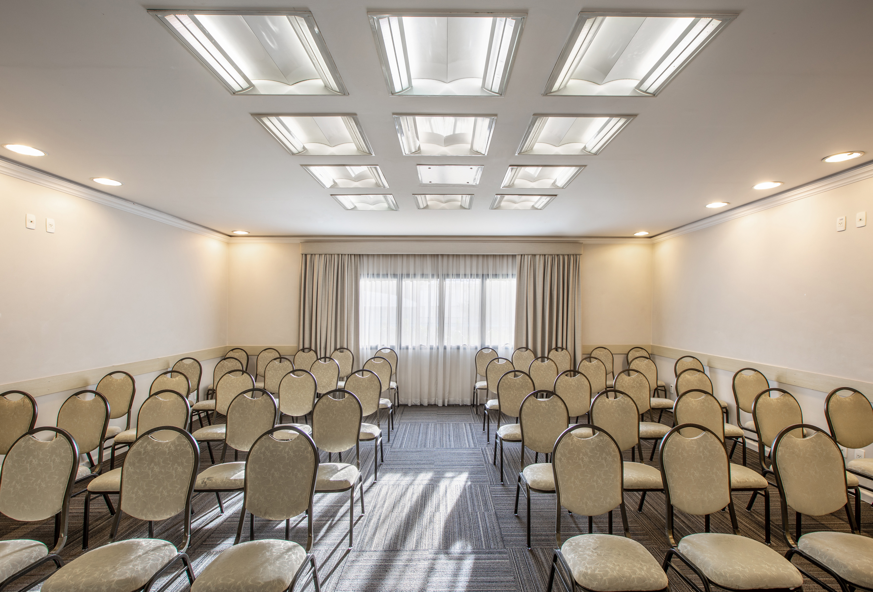 Empty meeting room with rows of chairs, striped carpet, and bright ceiling lights.
