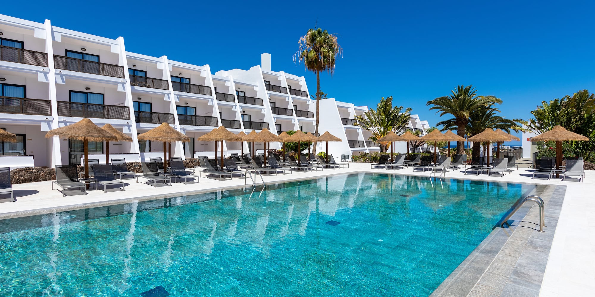 a pool with umbrellas and chairs in front of a building