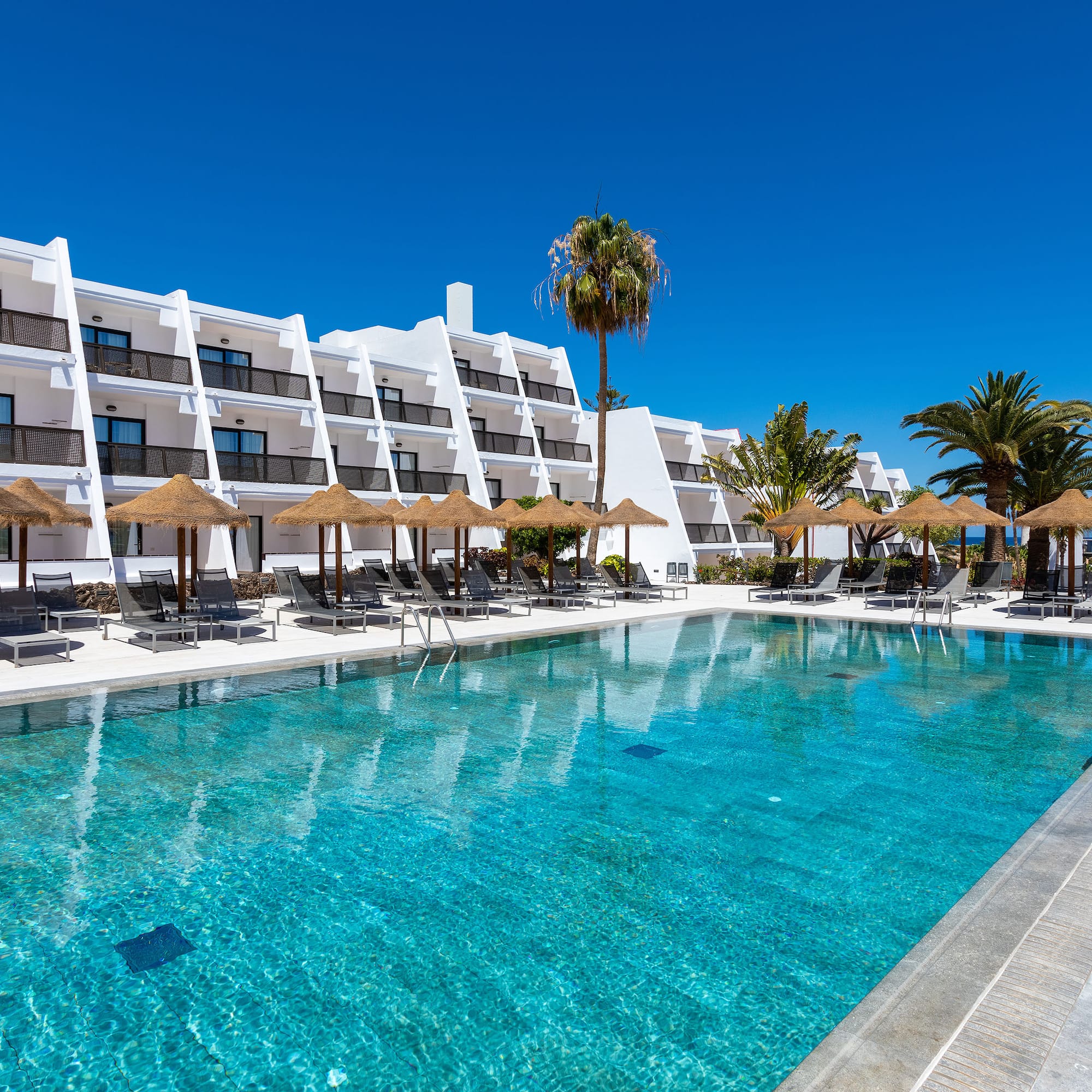 a pool with umbrellas and chairs in front of a building