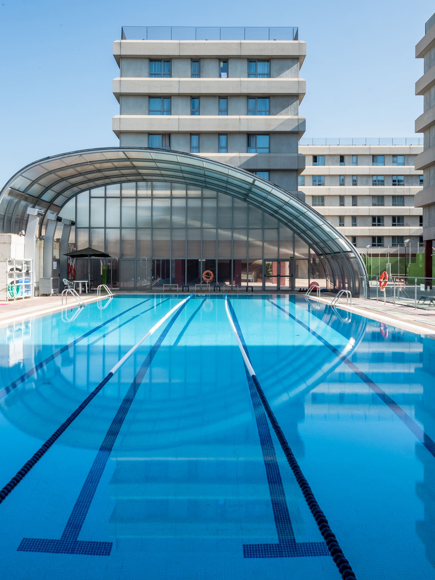 Piscina exterior con carriles, cubierta arqueada y edificios modernos.