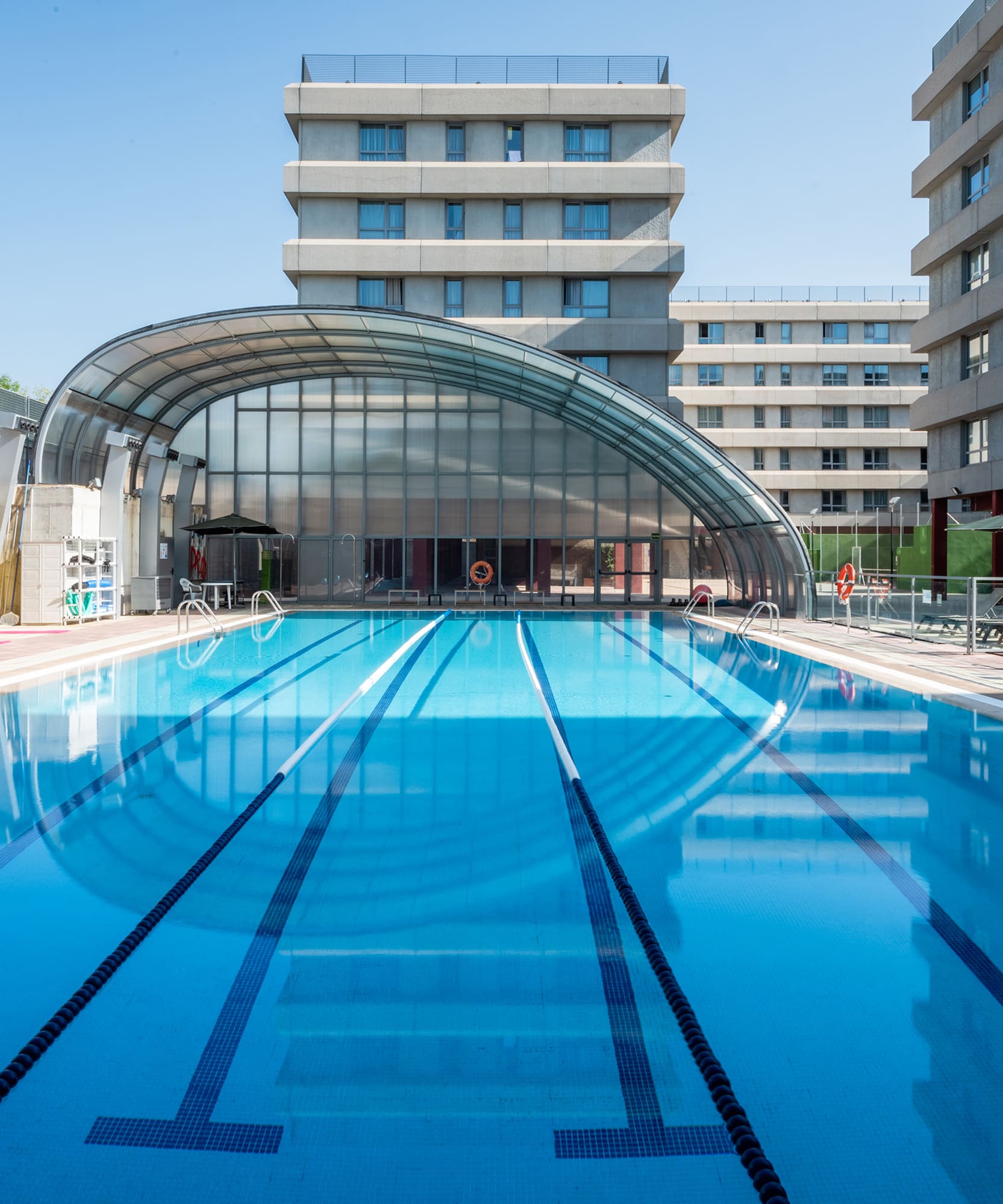Piscina exterior con carriles, cubierta arqueada y edificios modernos.