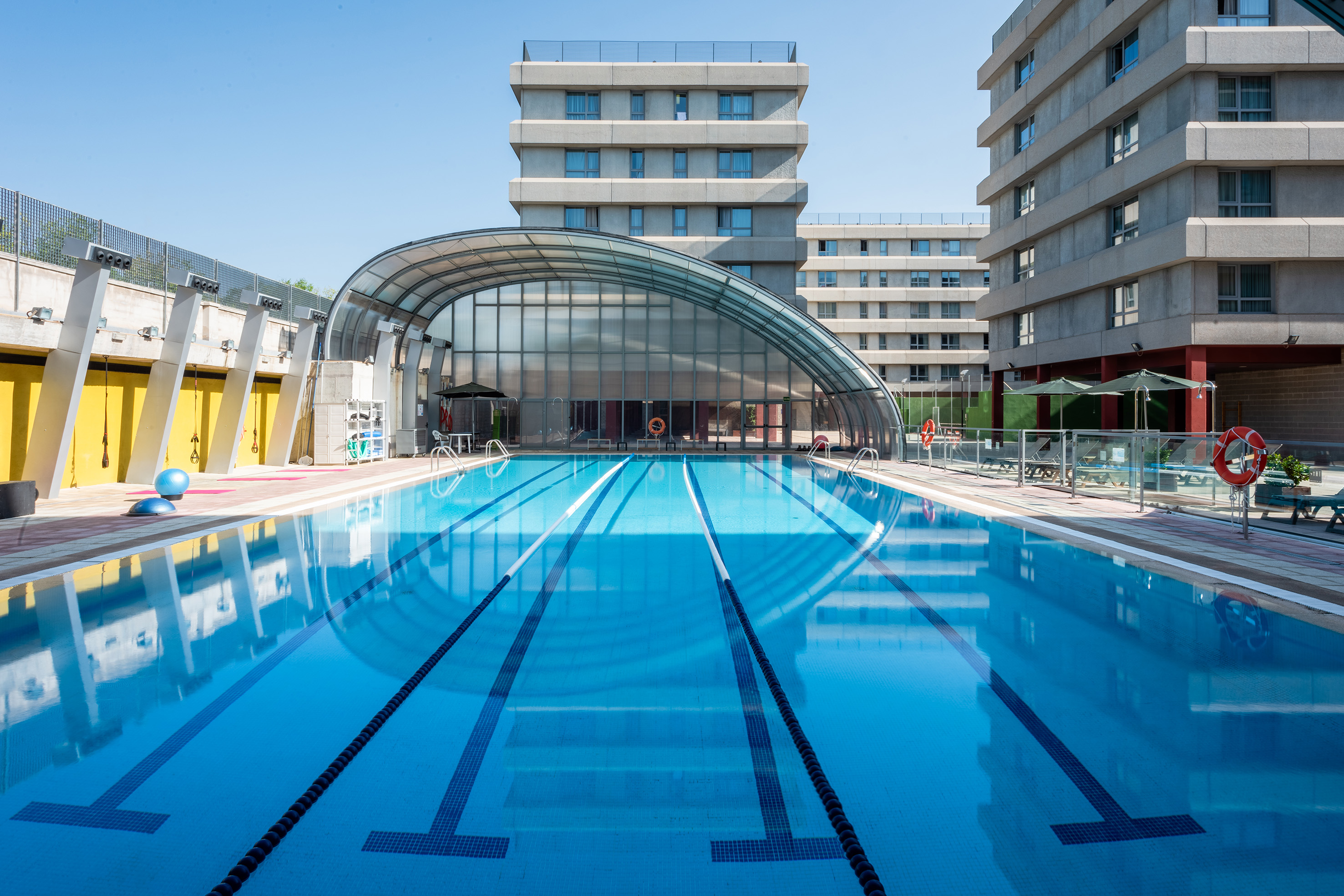 Piscina exterior con carriles, cubierta arqueada y edificios modernos.
