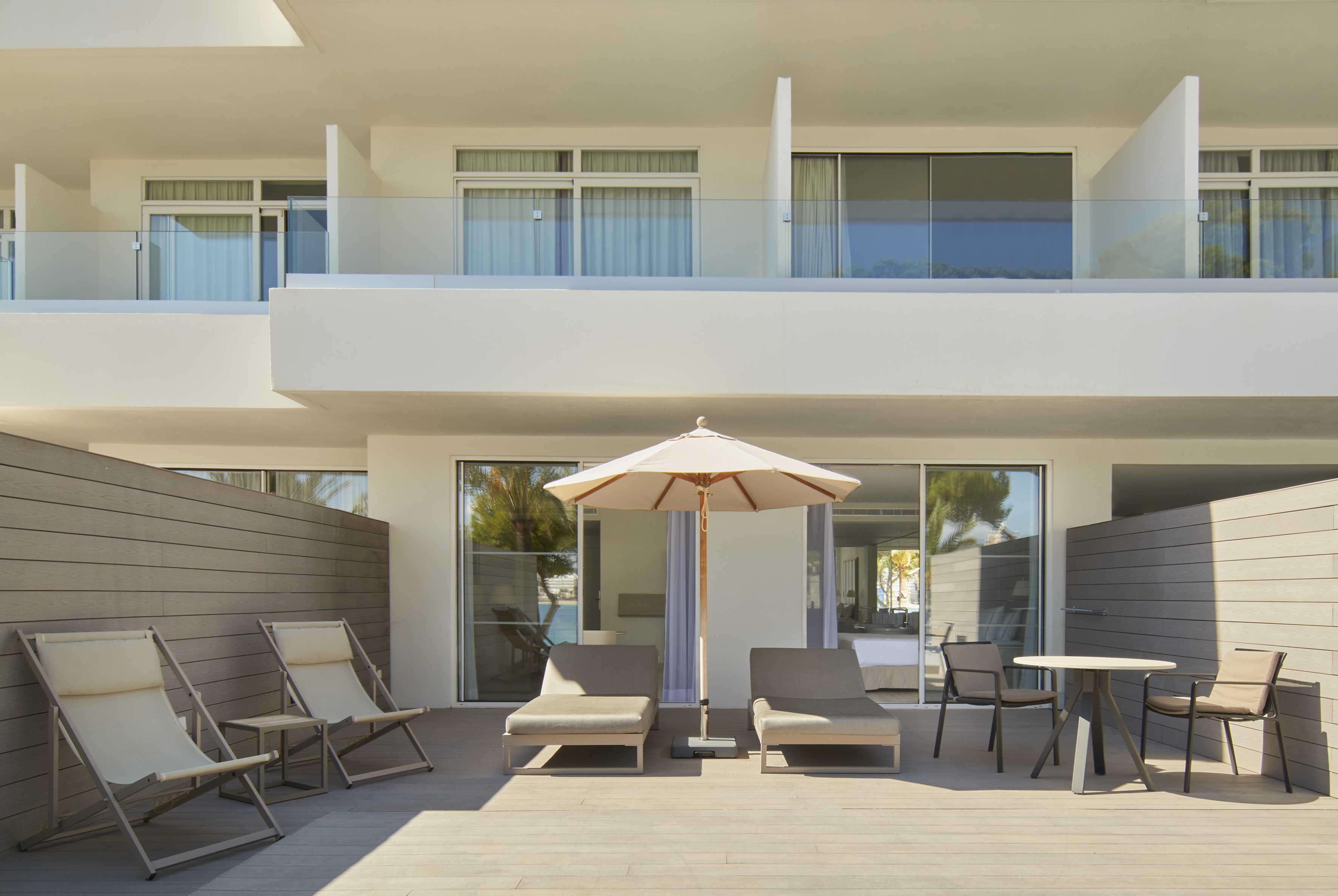 Modern hotel terrace with sun loungers, umbrella, and outdoor dining.