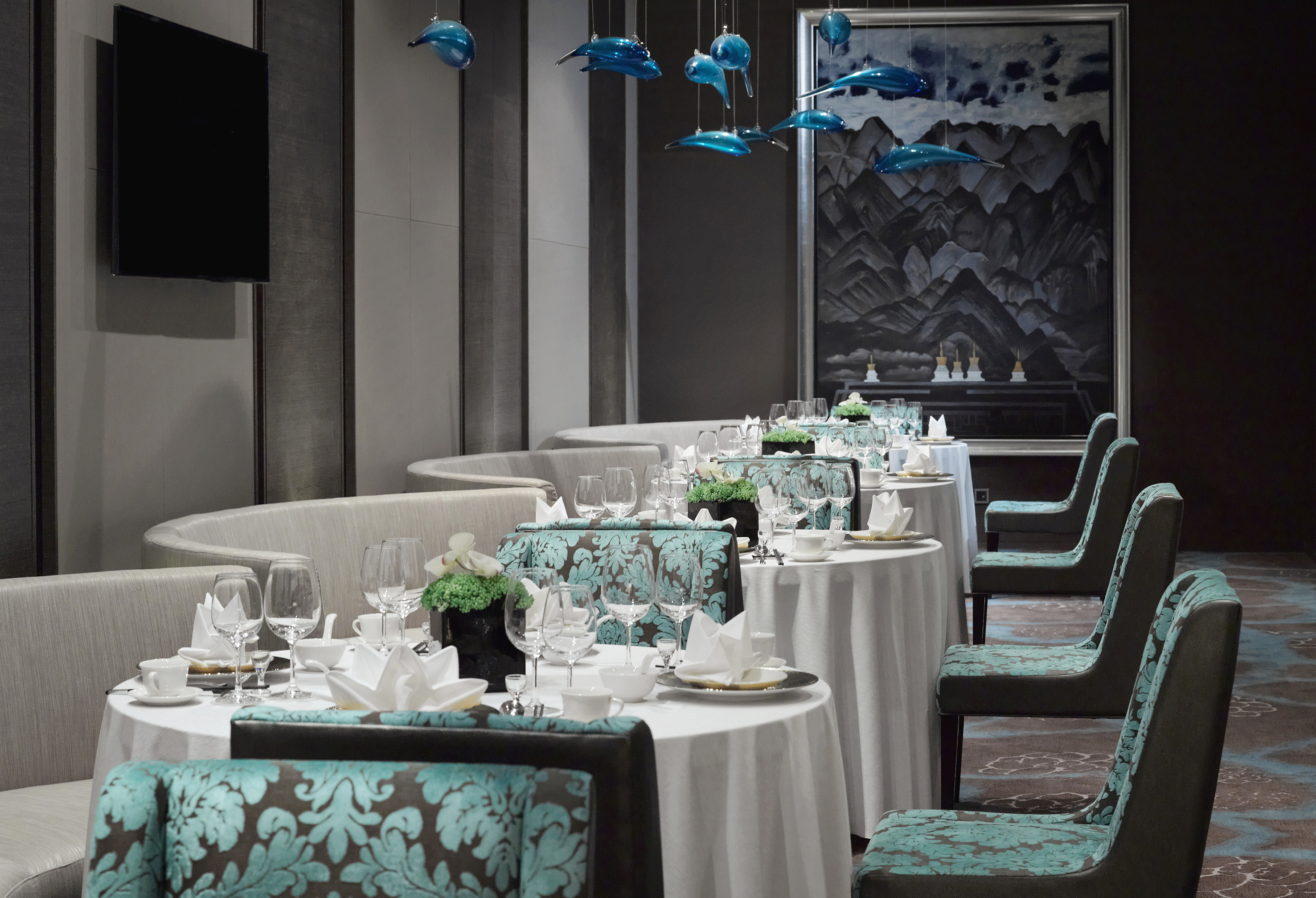 Elegant dining room with set tables, teal chairs, and blue glass fish decor.