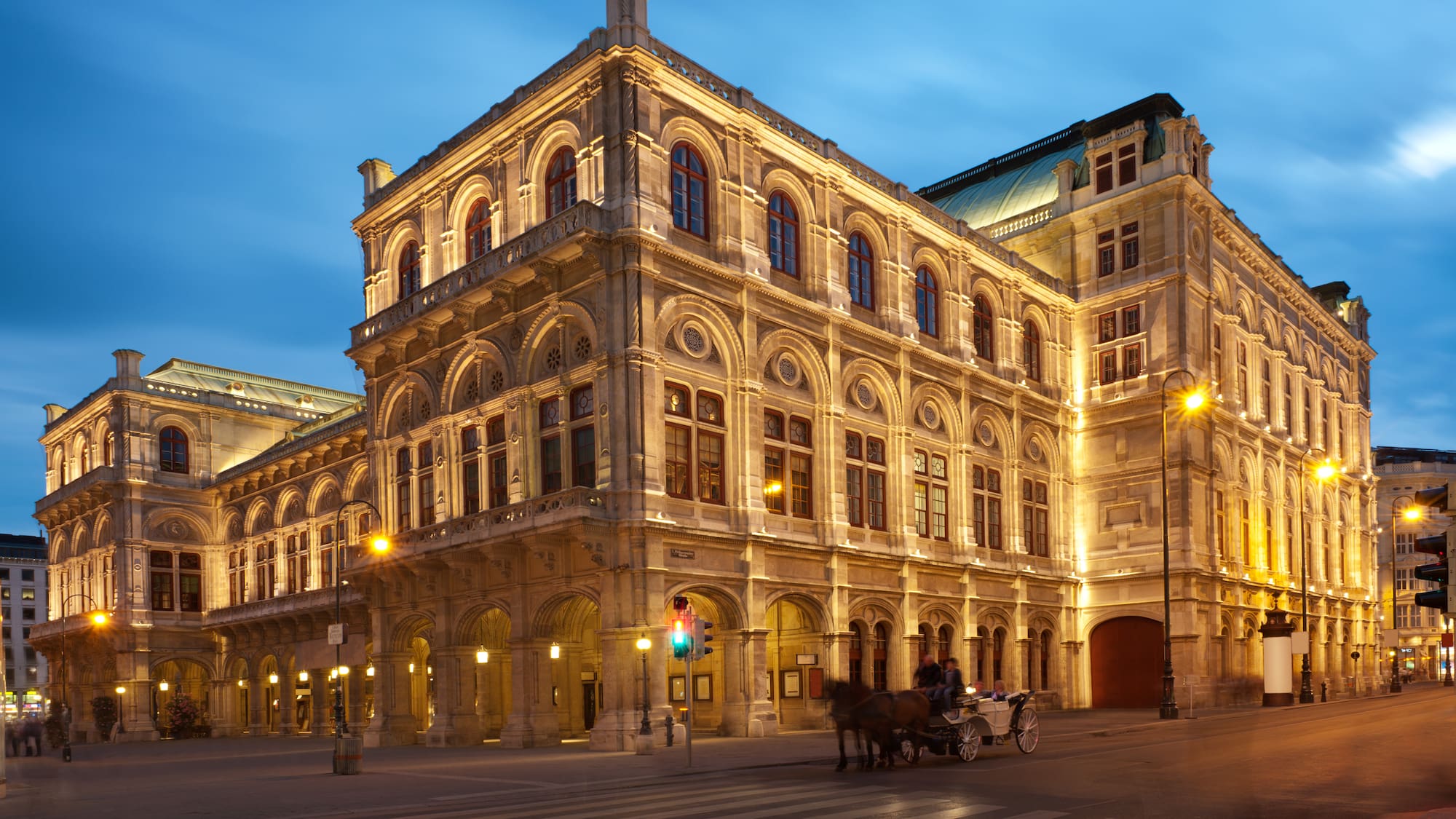 a large stone building with a horse drawn carriage on the side with Vienna State Opera in the background