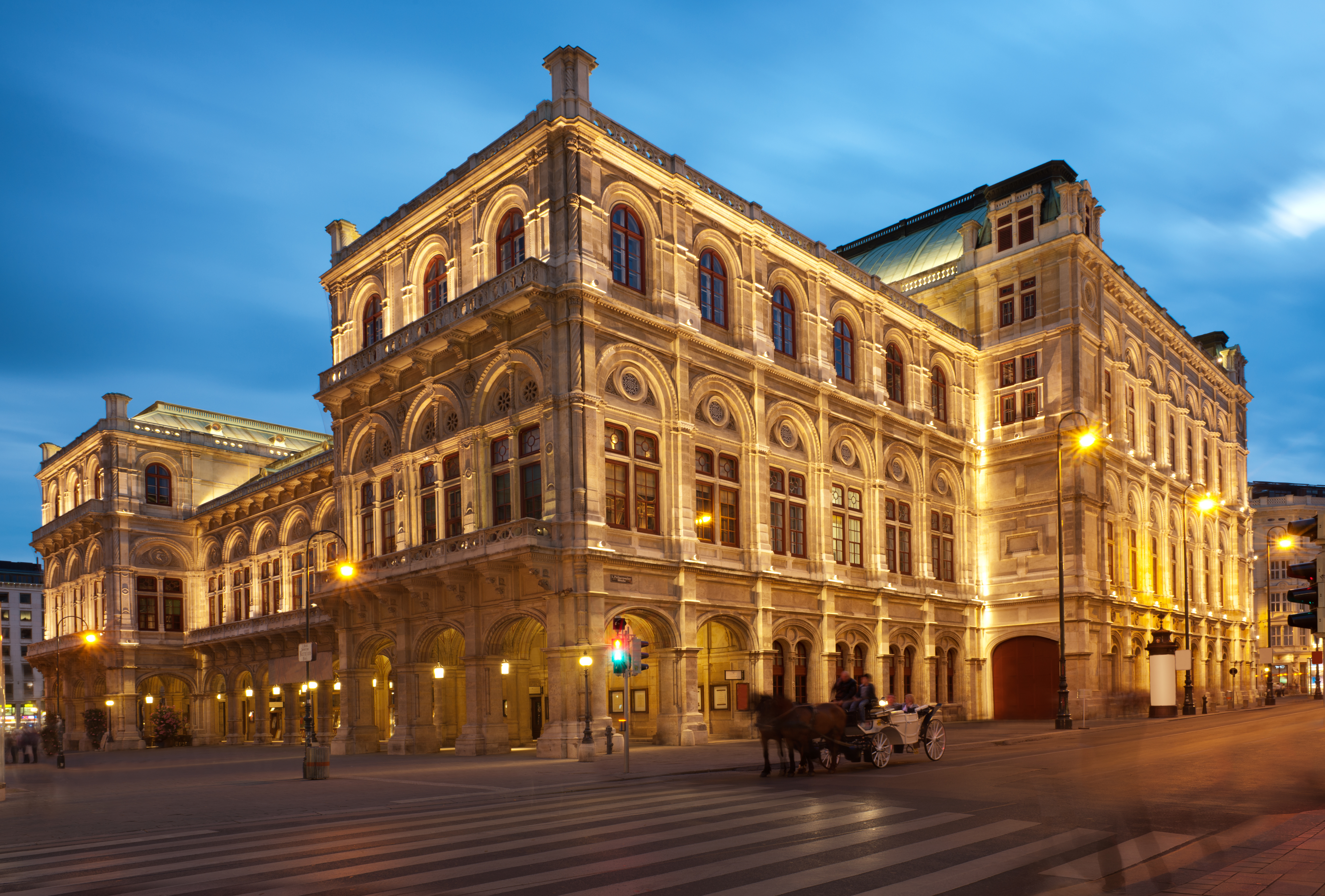 a large stone building with a horse drawn carriage on the side with Vienna State Opera in the background