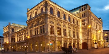 a large stone building with a horse drawn carriage on the side with Vienna State Opera in the background