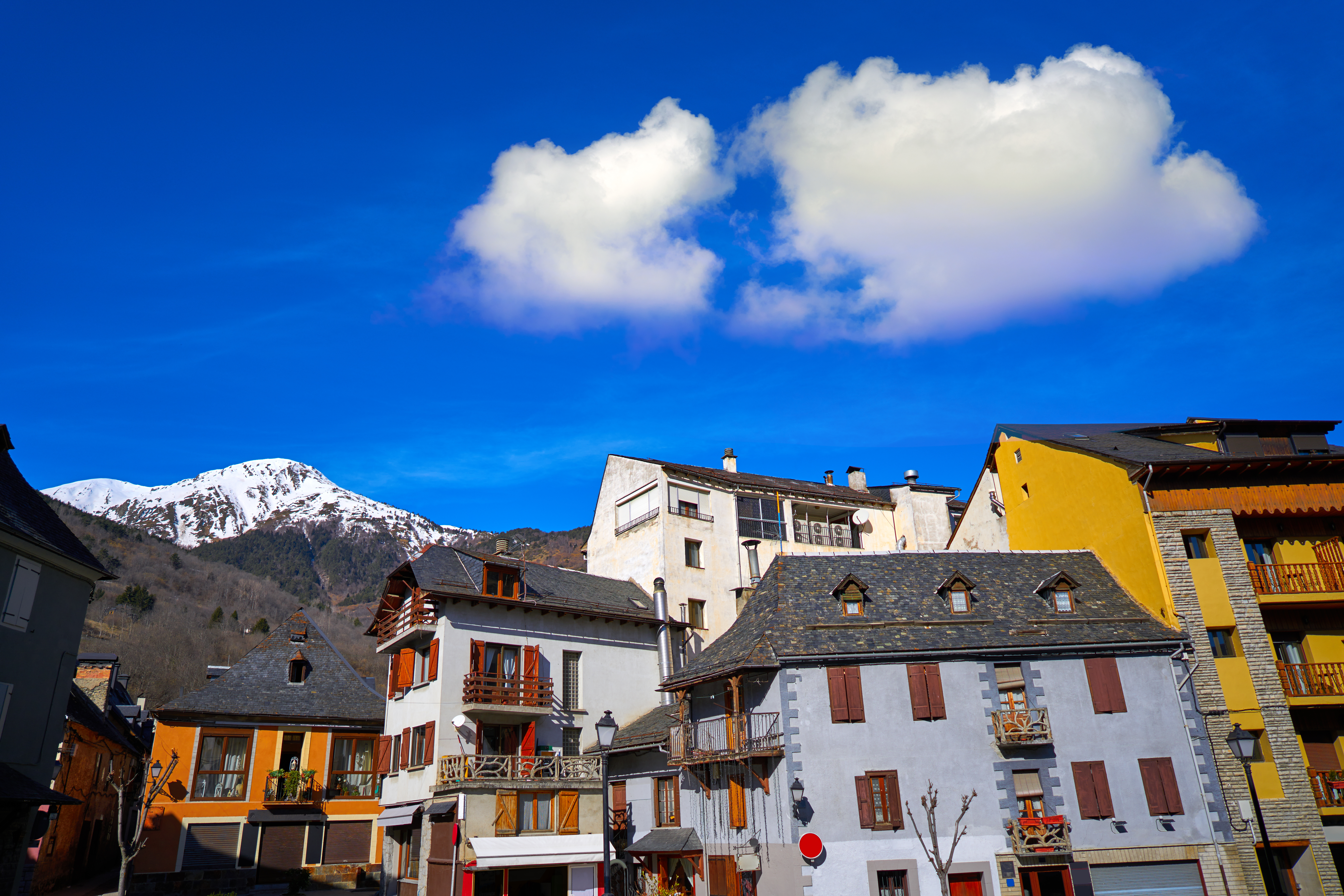 Colorful traditional houses in mountain village, snow-capped peak, blue sky.