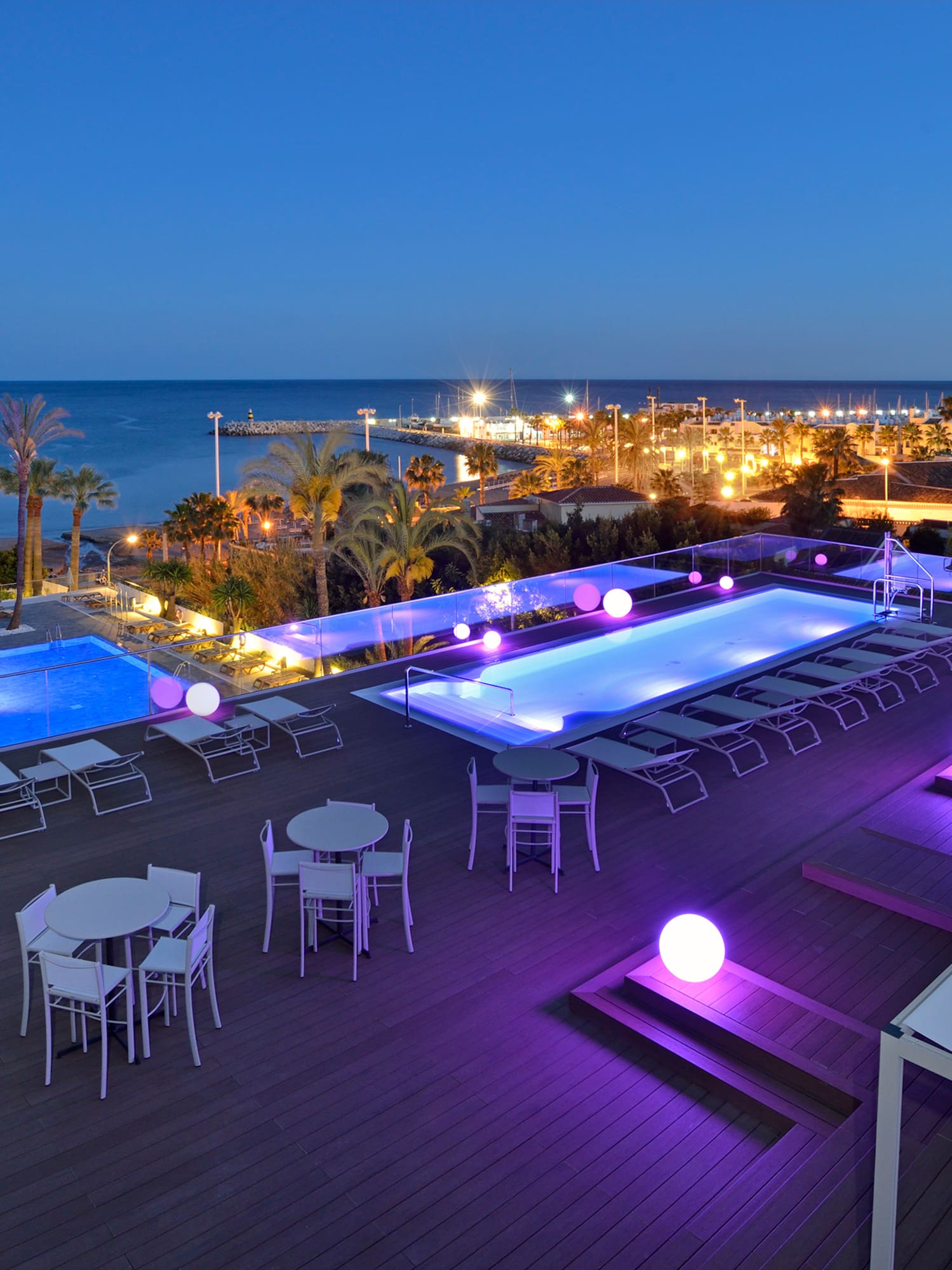 a pool and tables on a deck with a city in the background