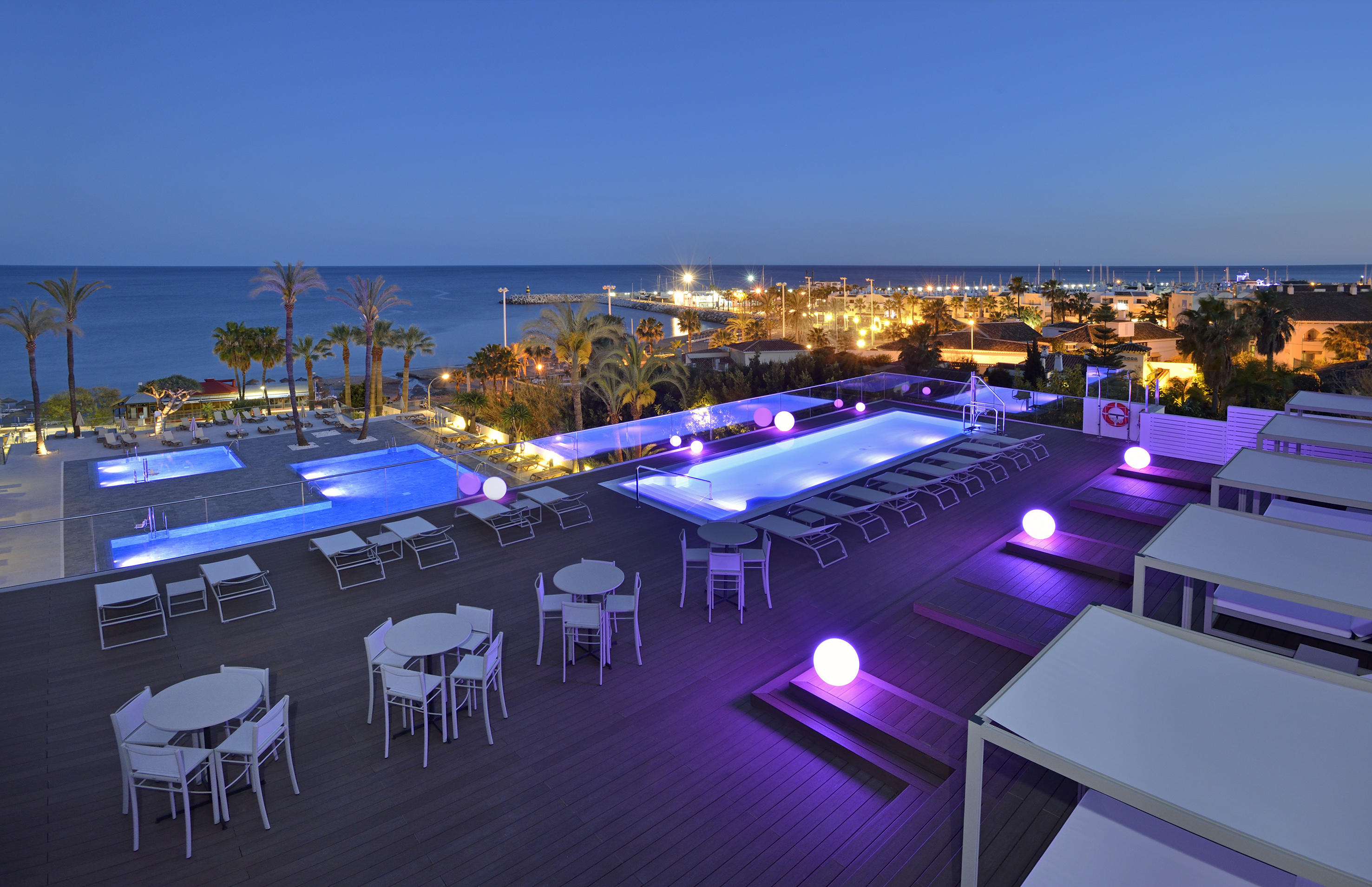 a pool and tables on a deck with a city in the background