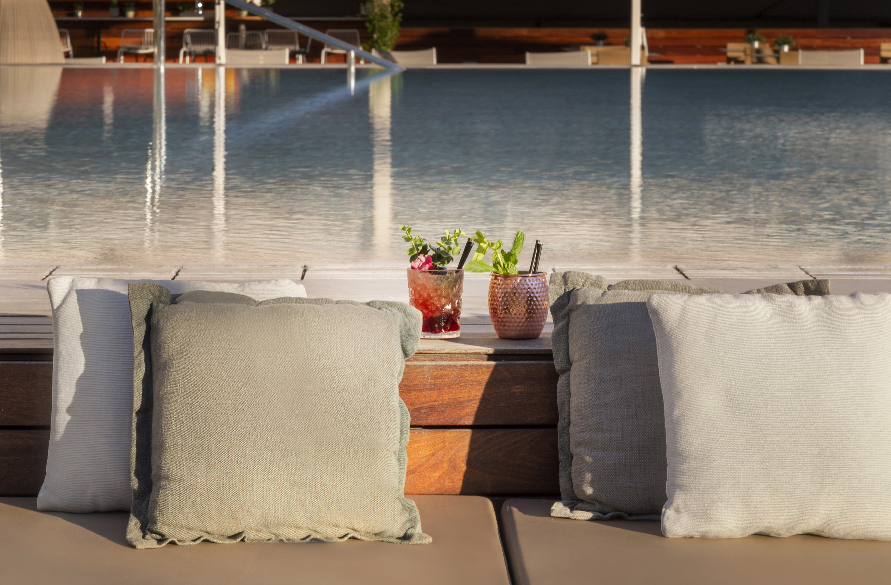 Cocktails on poolside daybed lounges, overlooking a resort swimming pool.