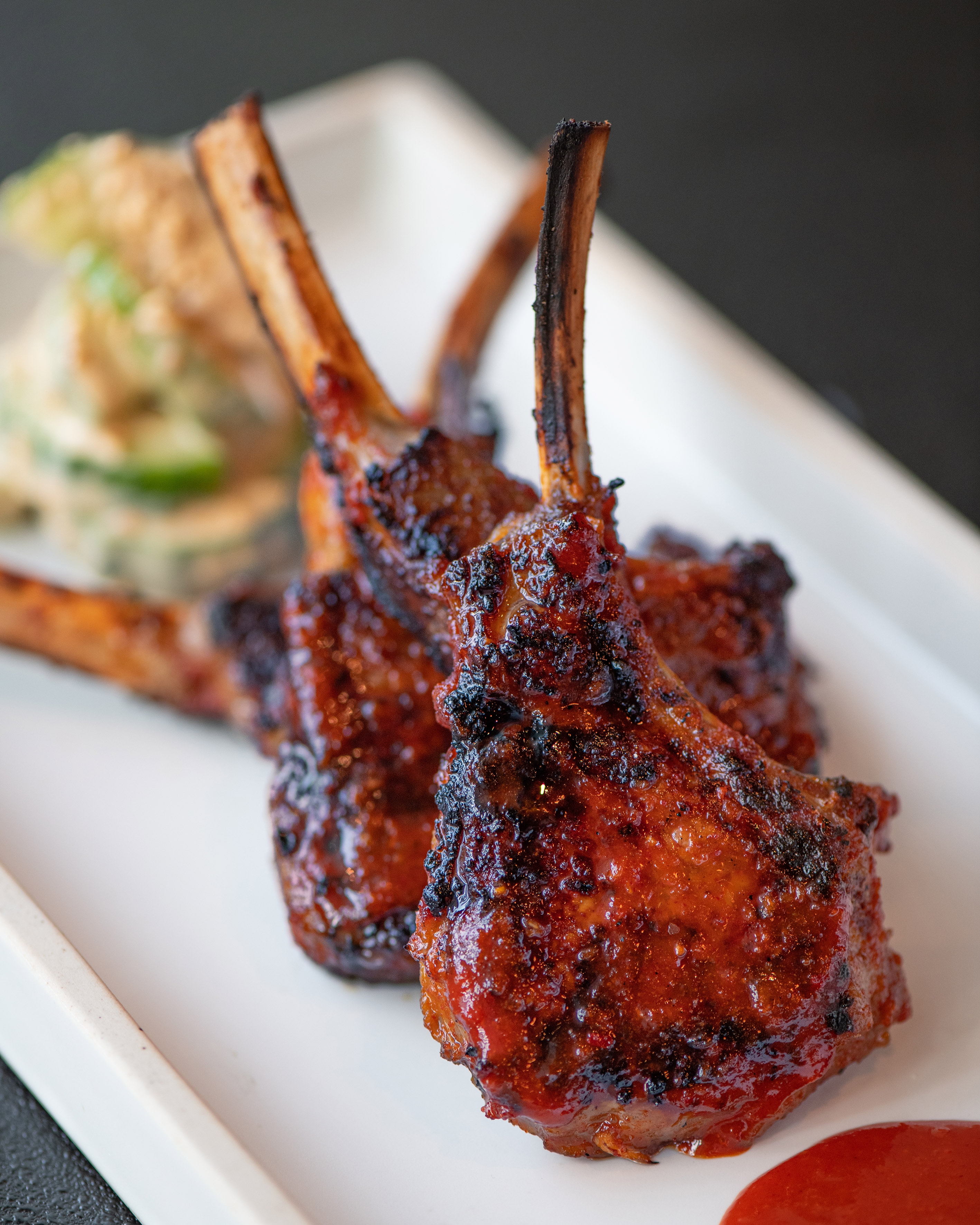 Grilled lamb chops with dark char, shiny BBQ glaze, and red sauce.