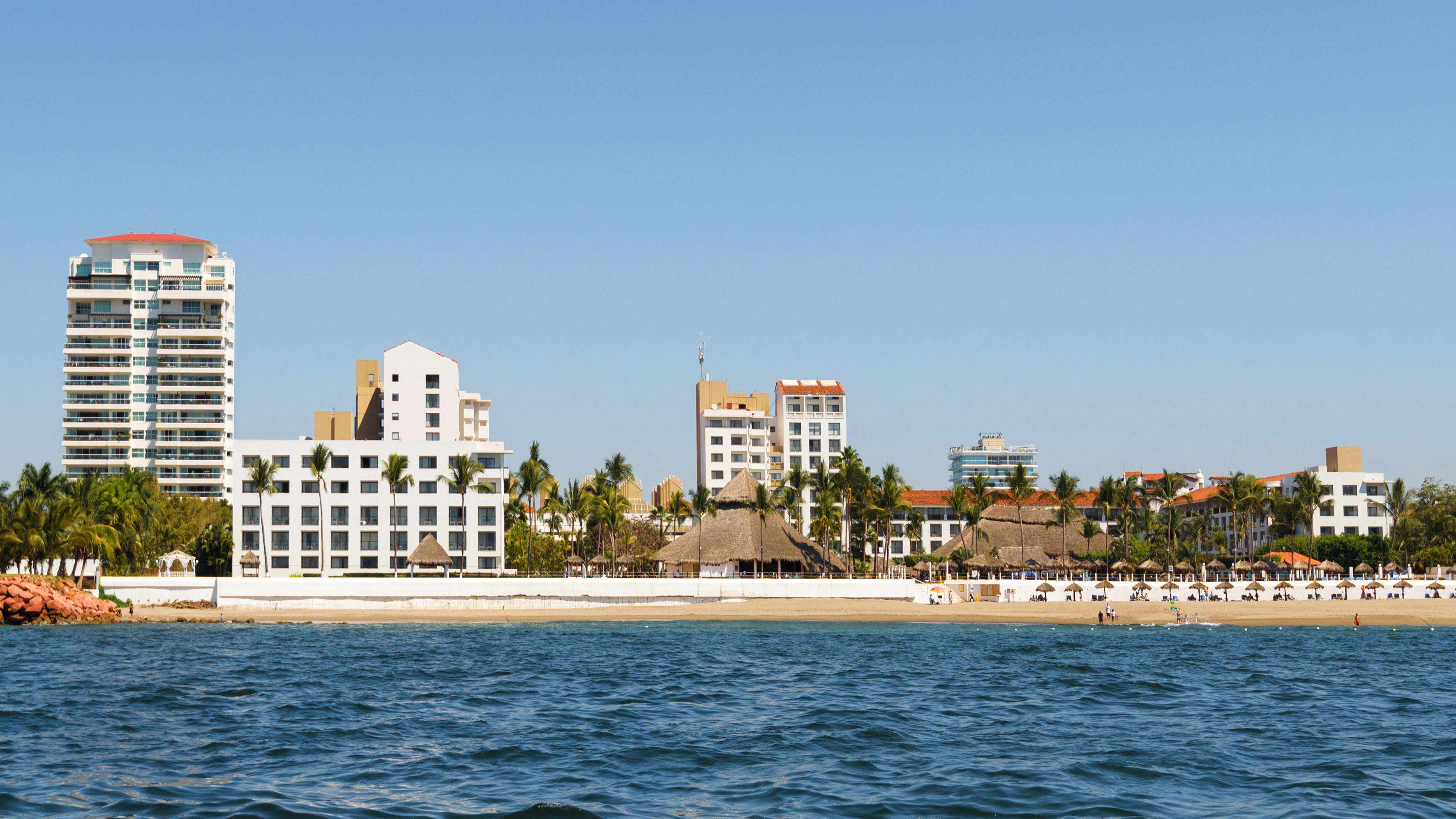 Tropical beach resort with hotels, palm trees, and palapas along the oceanfront.