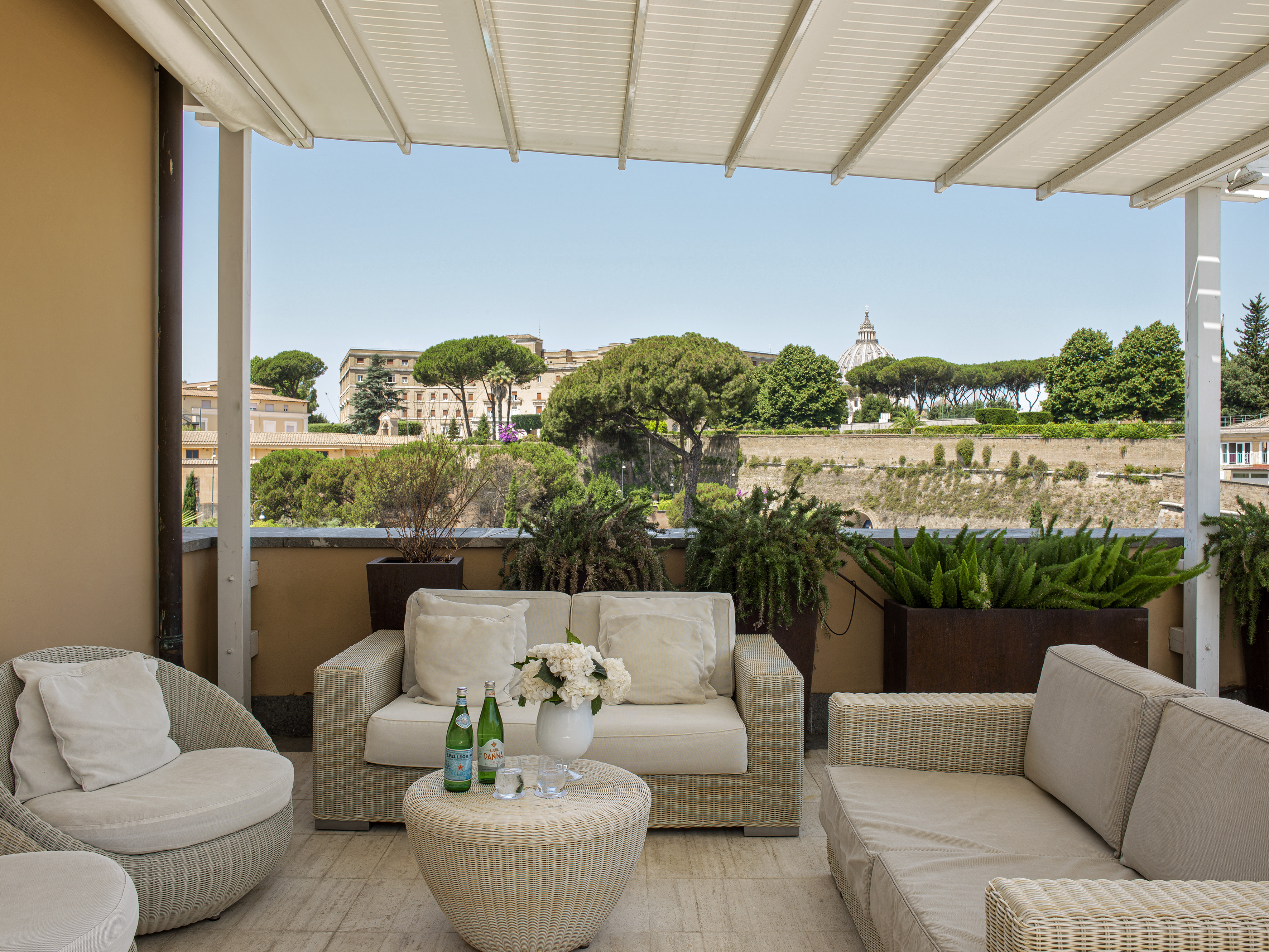 Rome rooftop terrace with wicker furniture, city view, and St. Peter's dome.
