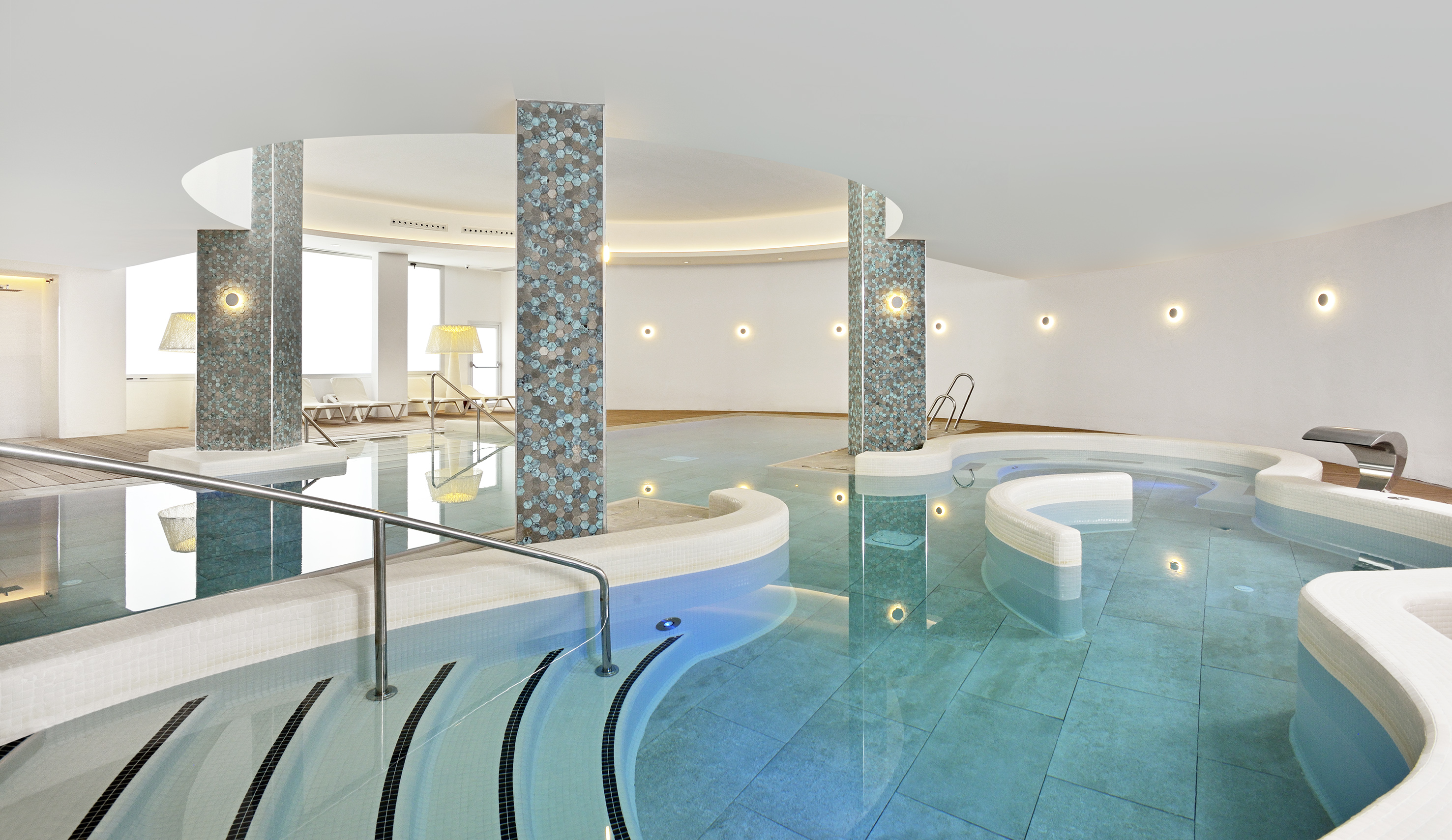 Indoor spa pool with blue water, mosaic pillars, and modern ambient lighting.