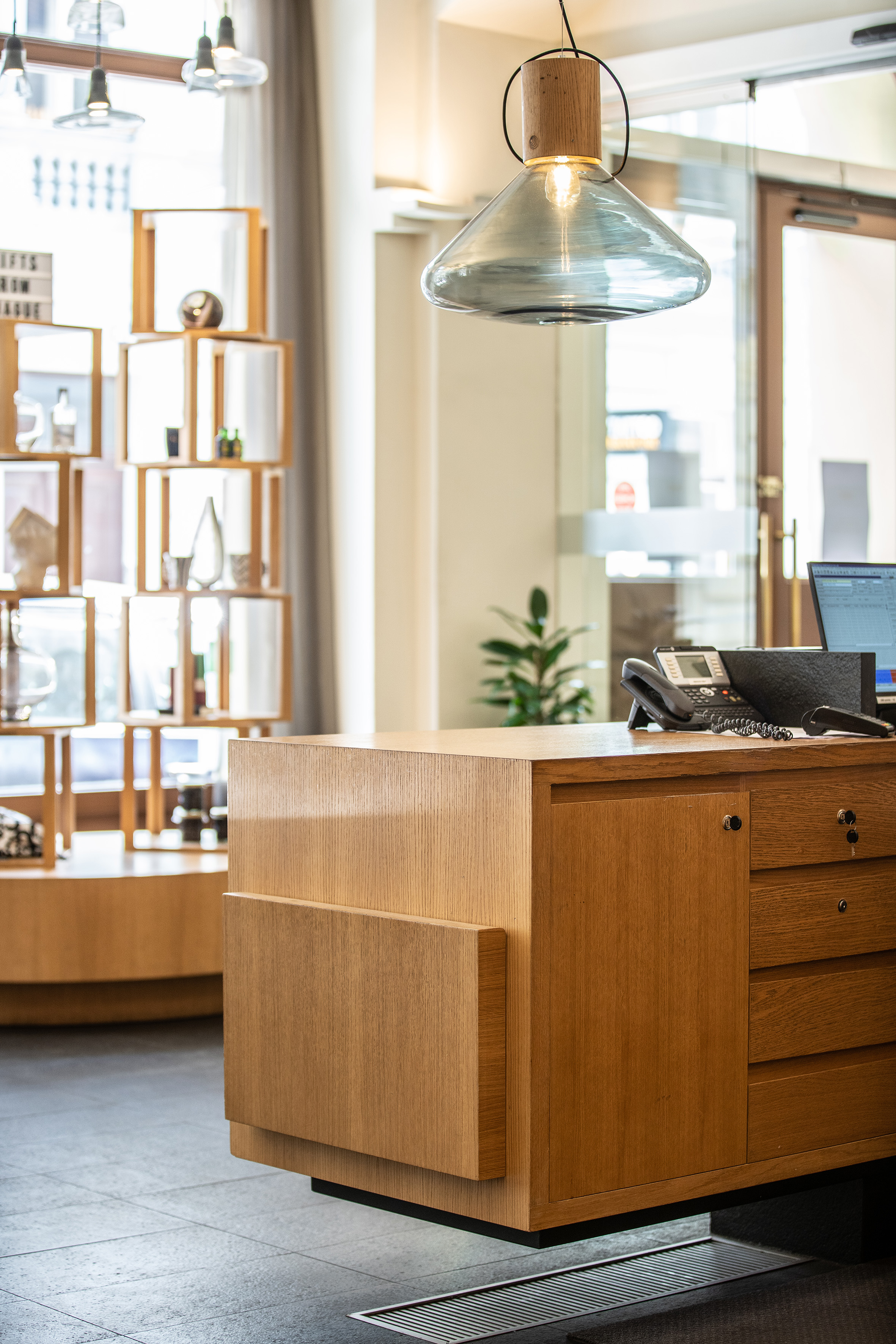 Modern wooden reception desk with phone, computer, and elegant pendant lamp.