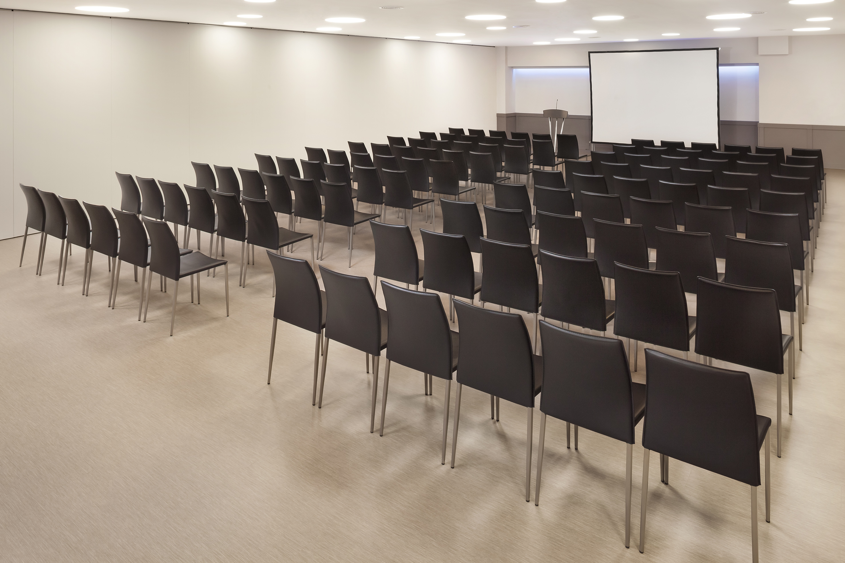 Large empty conference room with black chairs, projection screen, and podium.