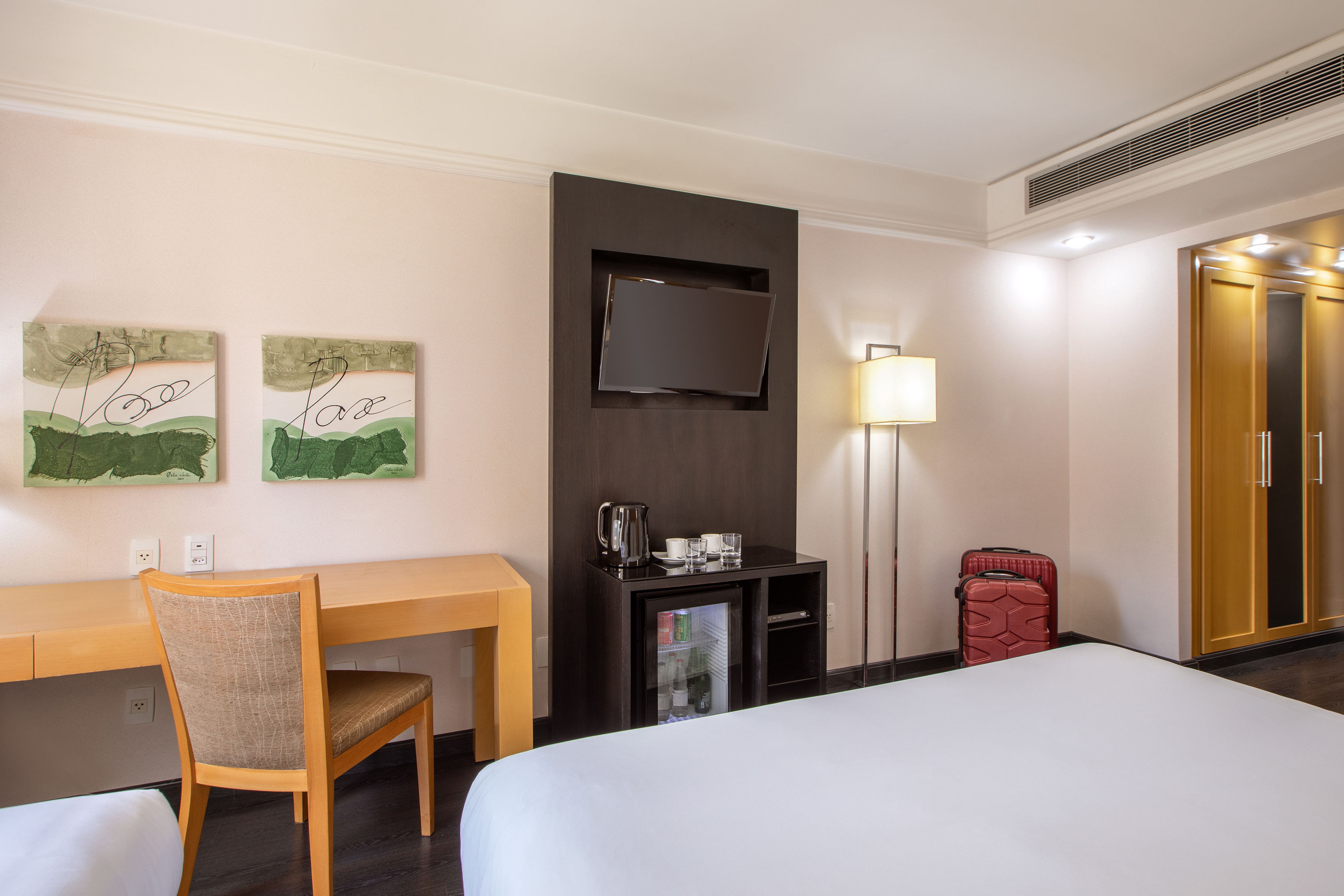Modern hotel room with bed, desk, flat-screen TV, minibar, and wardrobe.