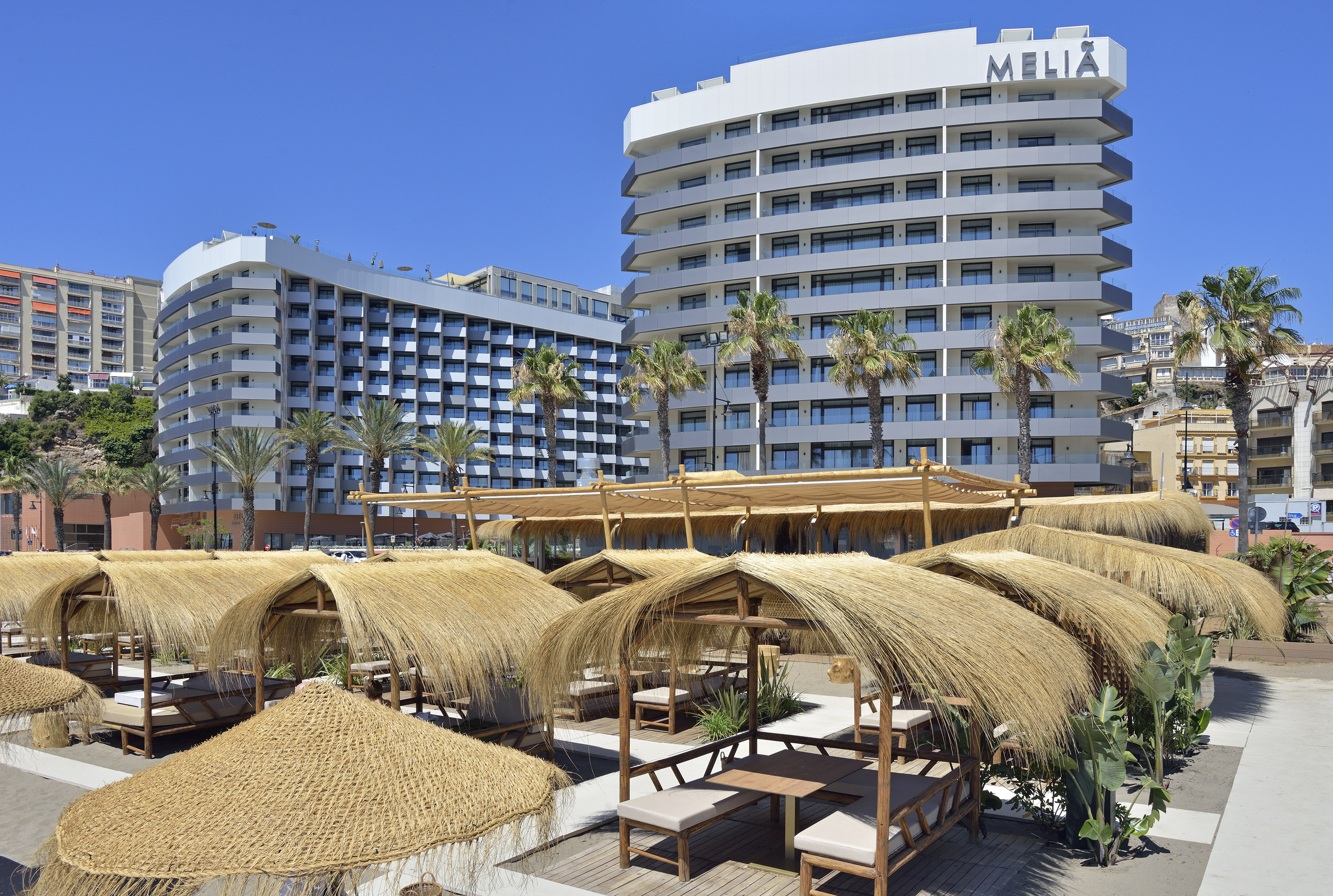 Melia hotel beachfront resort with palm trees and straw cabanas under blue sky.