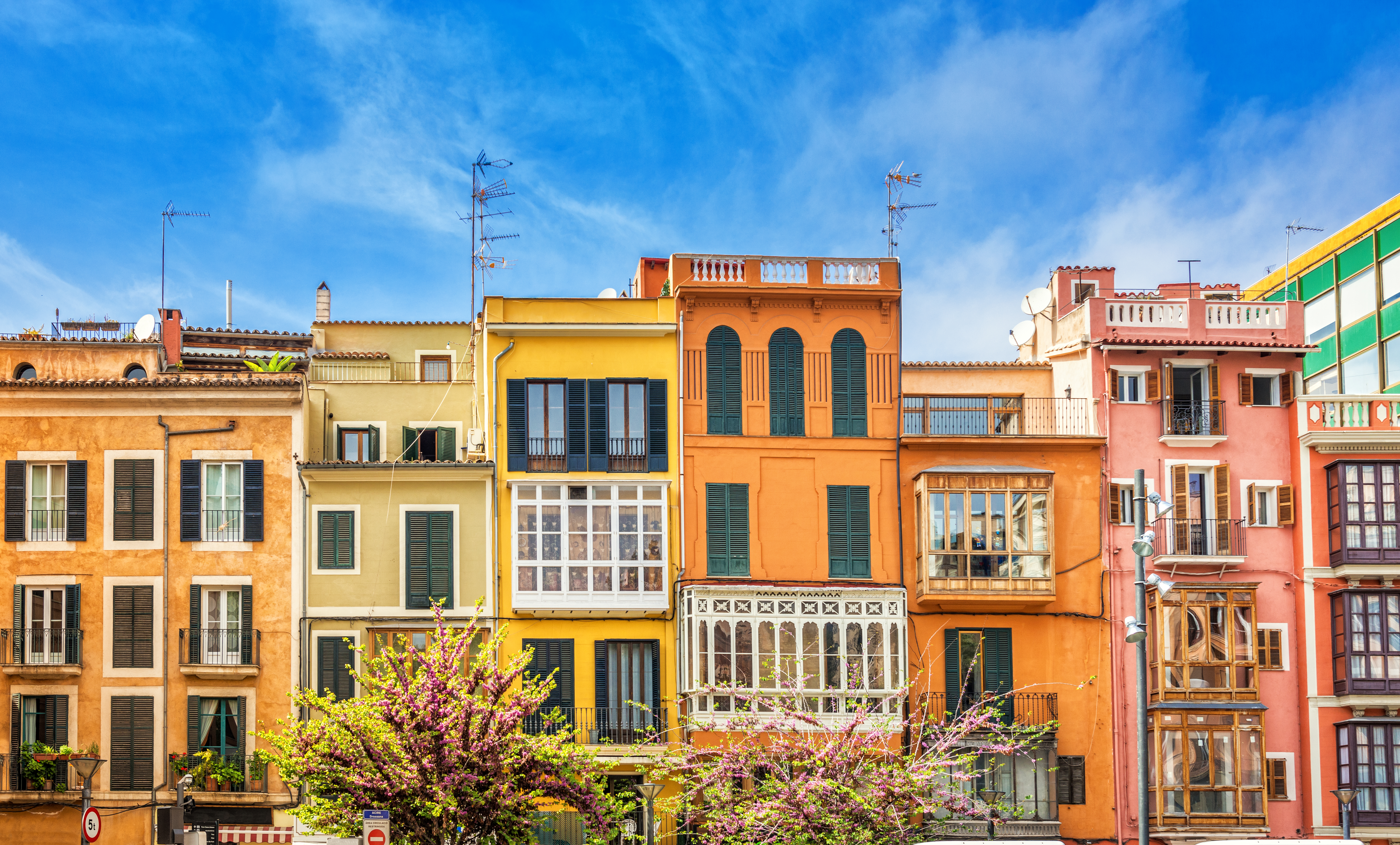 Vibrant colorful European city buildings with balconies and flowering trees.