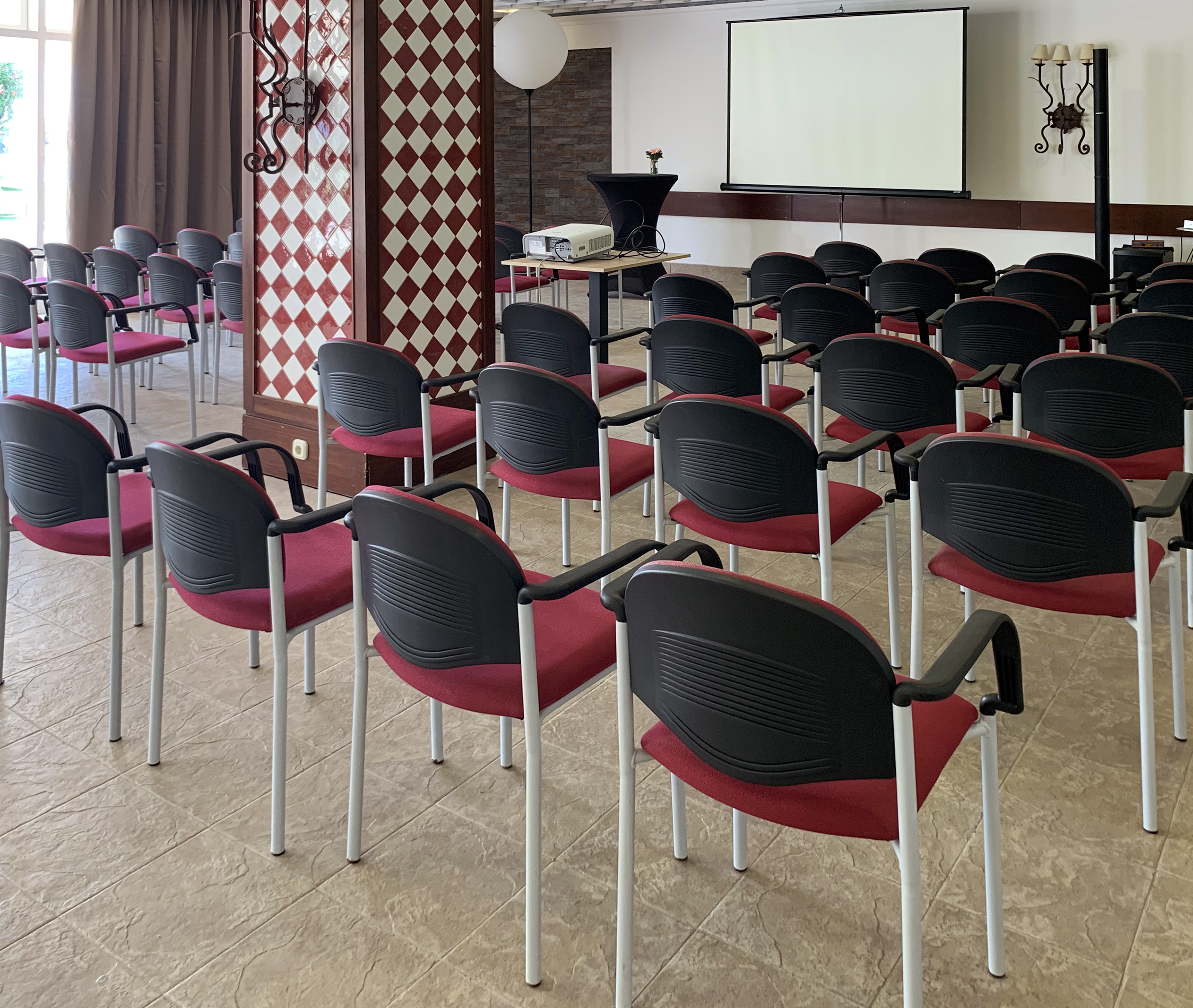 Conference room setup with red chairs, projector, and large screen for meetings or events.