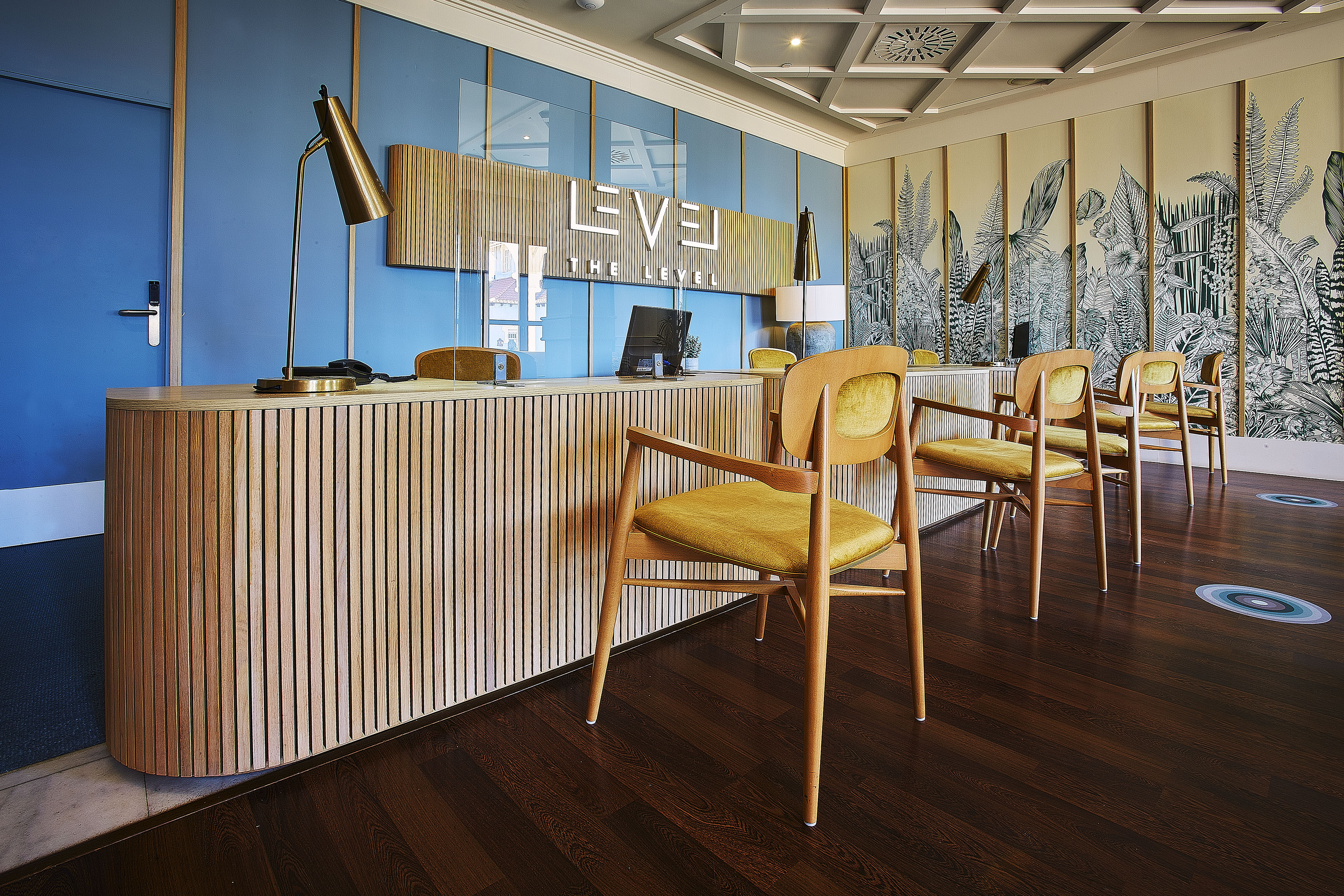 THE LEVEL hotel reception with wooden desk, blue wall, and botanical mural.