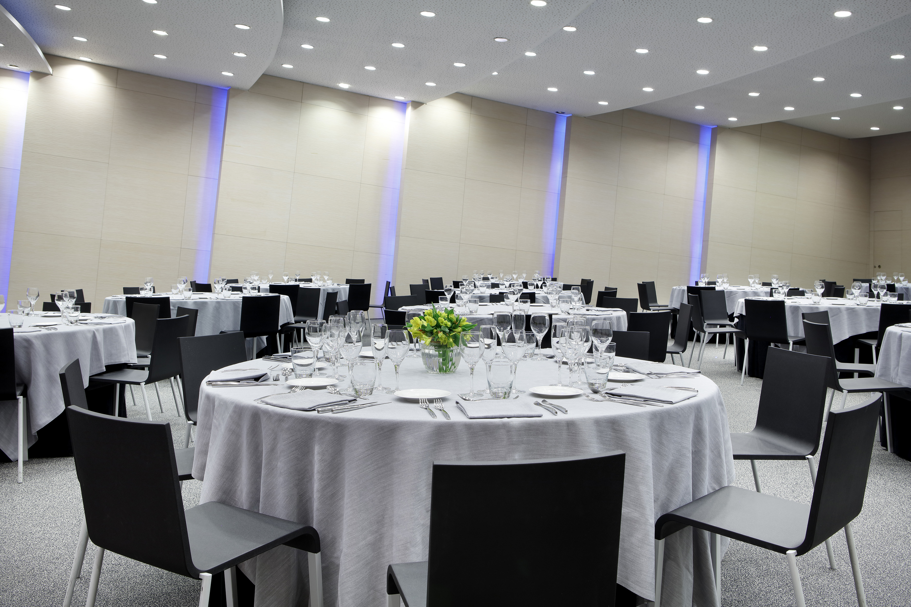 Modern conference room with set round tables, black chairs, and blue wall lighting.