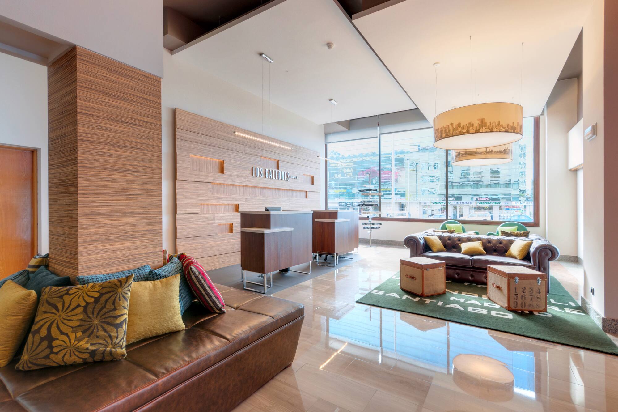 Modern hotel lobby with wooden reception, brown leather seating, and large windows.