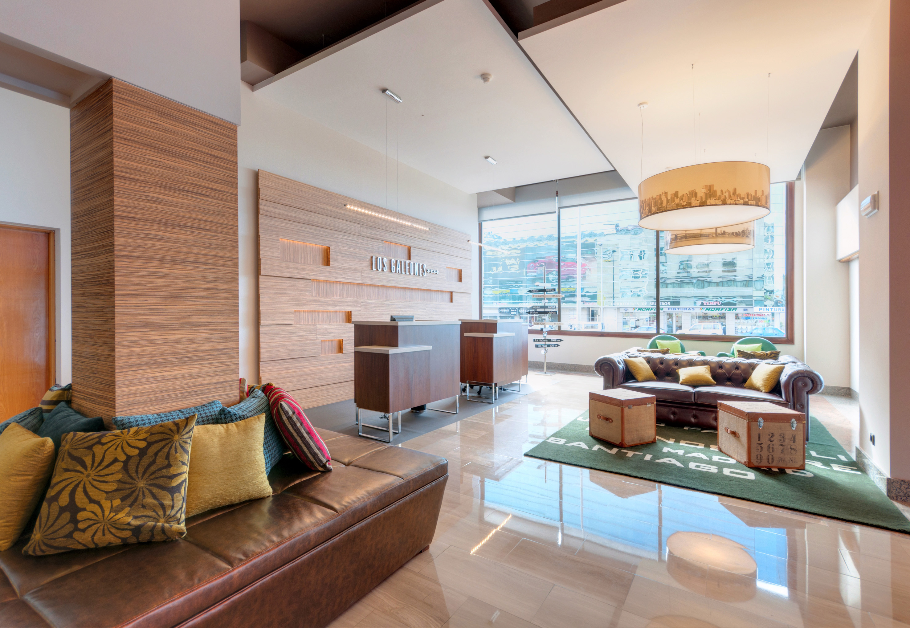 Modern hotel lobby with wooden reception, brown leather seating, and large windows.