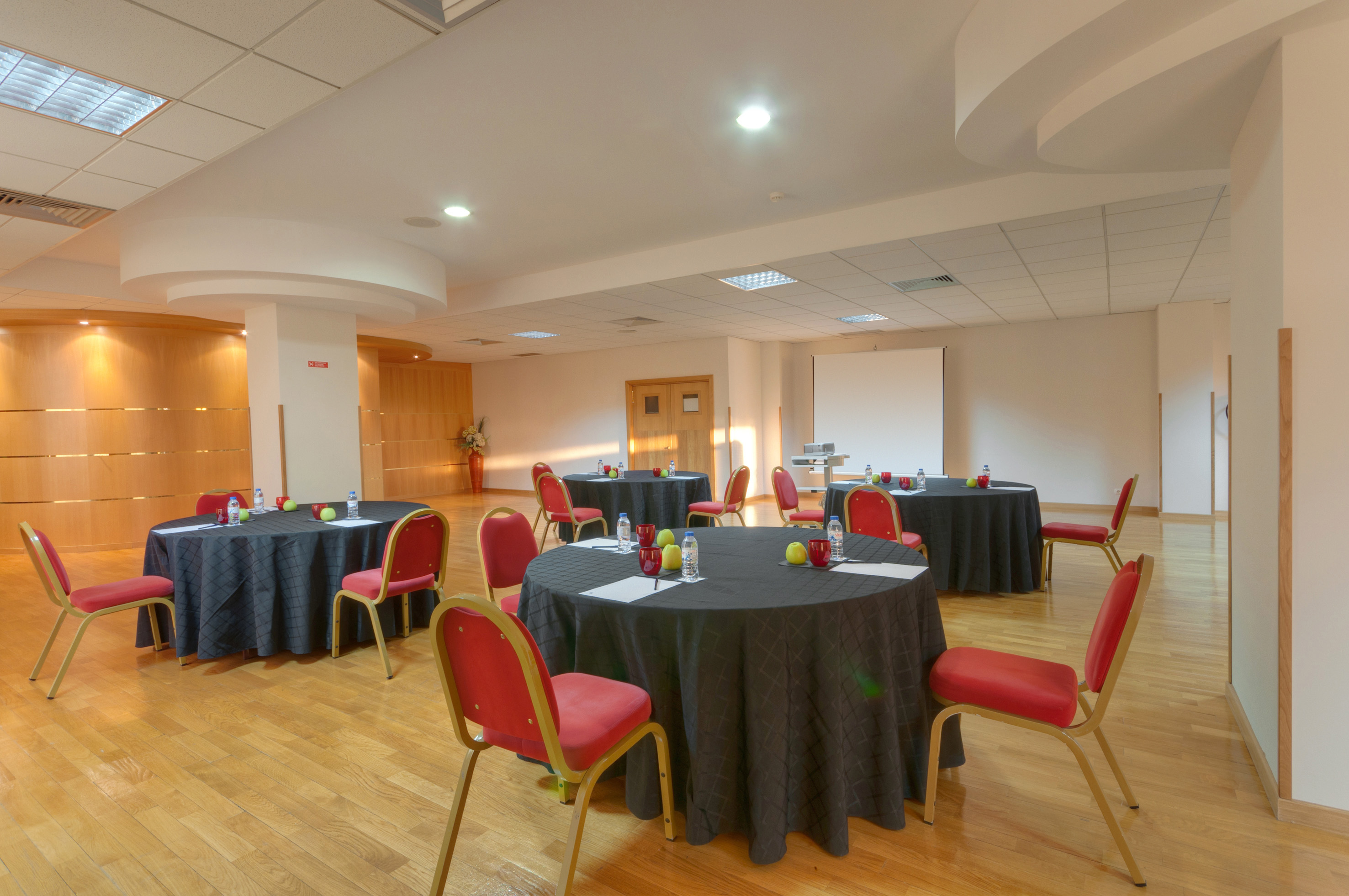 Conference room with black round tables, red chairs, presentation screen.