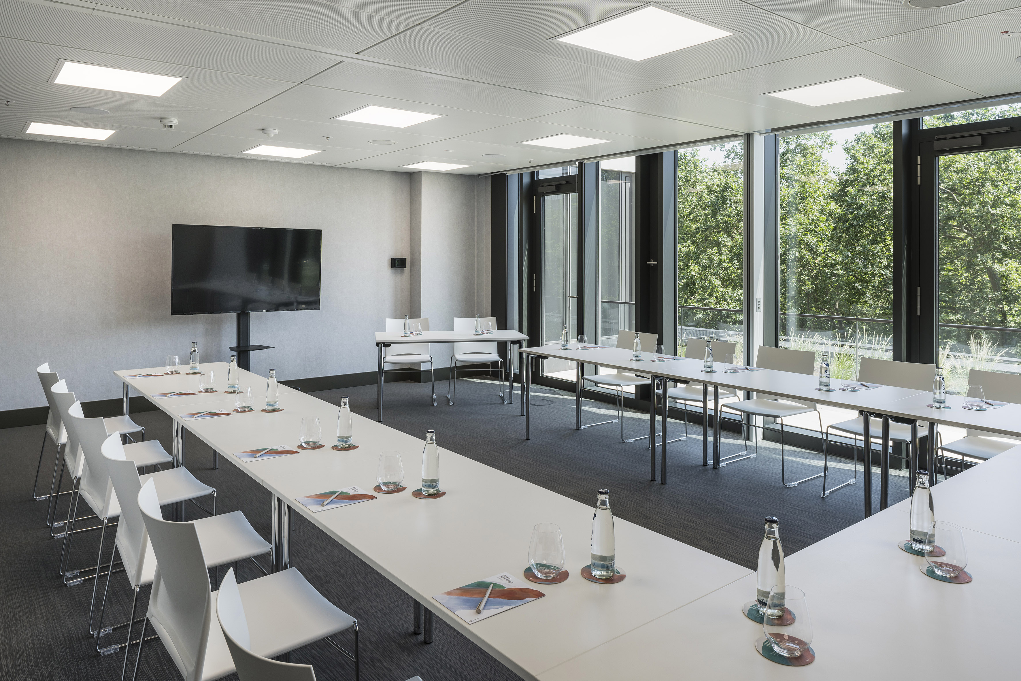 Modern meeting room with U-shaped table, TV, and large windows.
