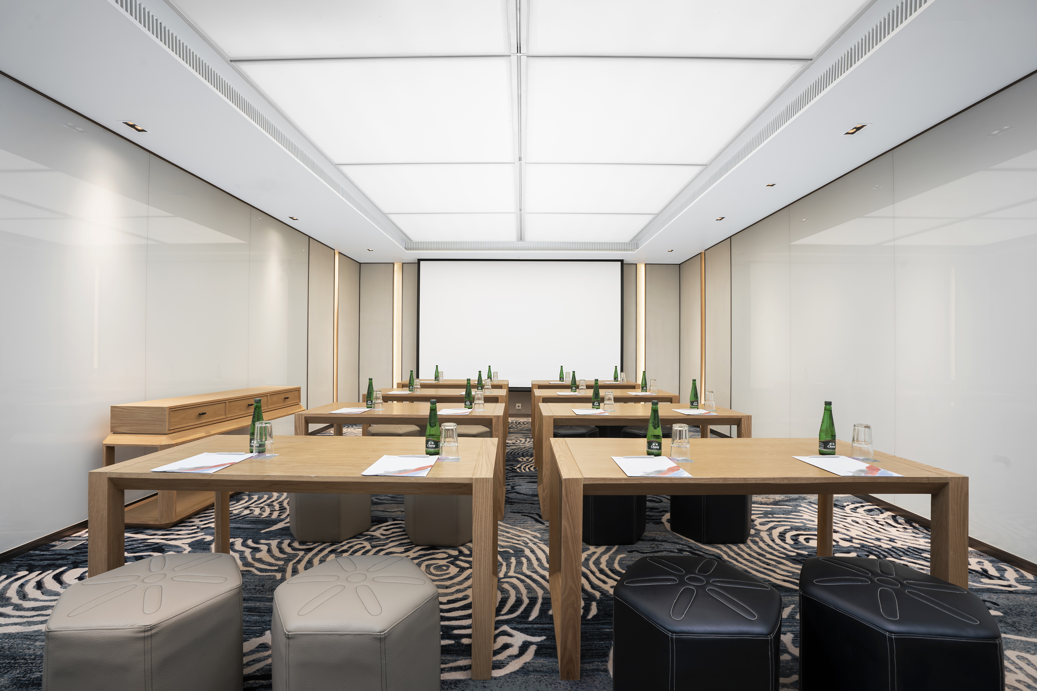 Modern meeting room with wood tables, pouf seating, and projection screen.