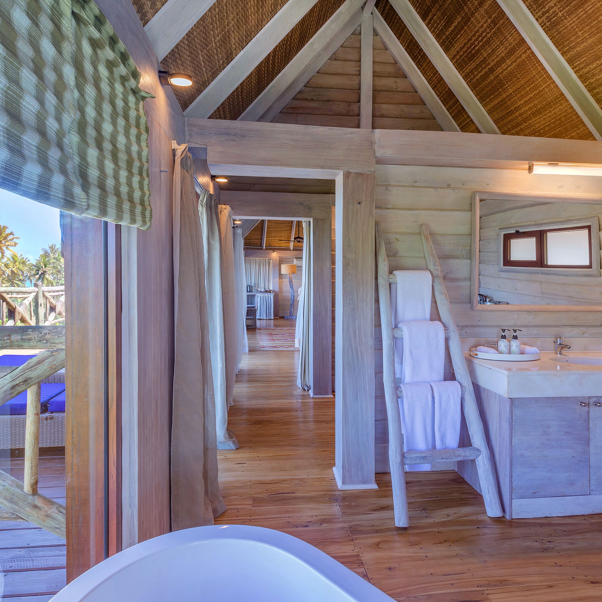 Tropical wooden bathroom in a villa with ocean view, palm trees, and vanity.