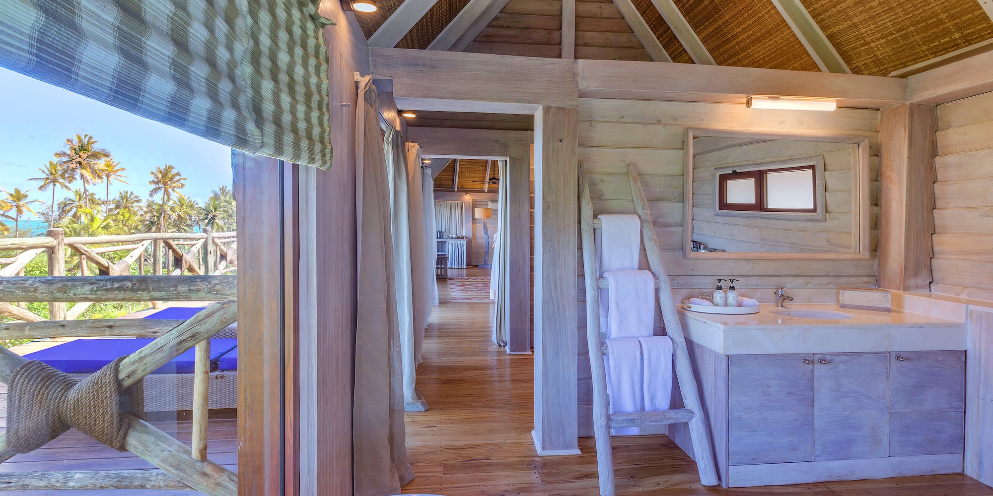 Tropical wooden bathroom in a villa with ocean view, palm trees, and vanity.