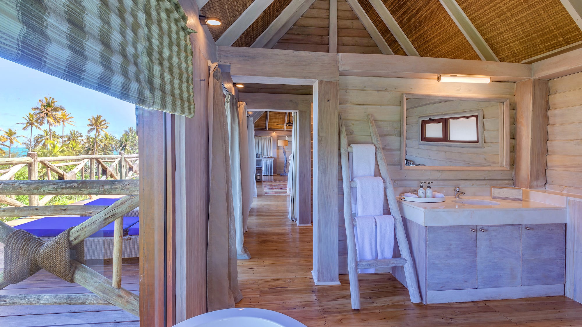 Tropical wooden bathroom in a villa with ocean view, palm trees, and vanity.