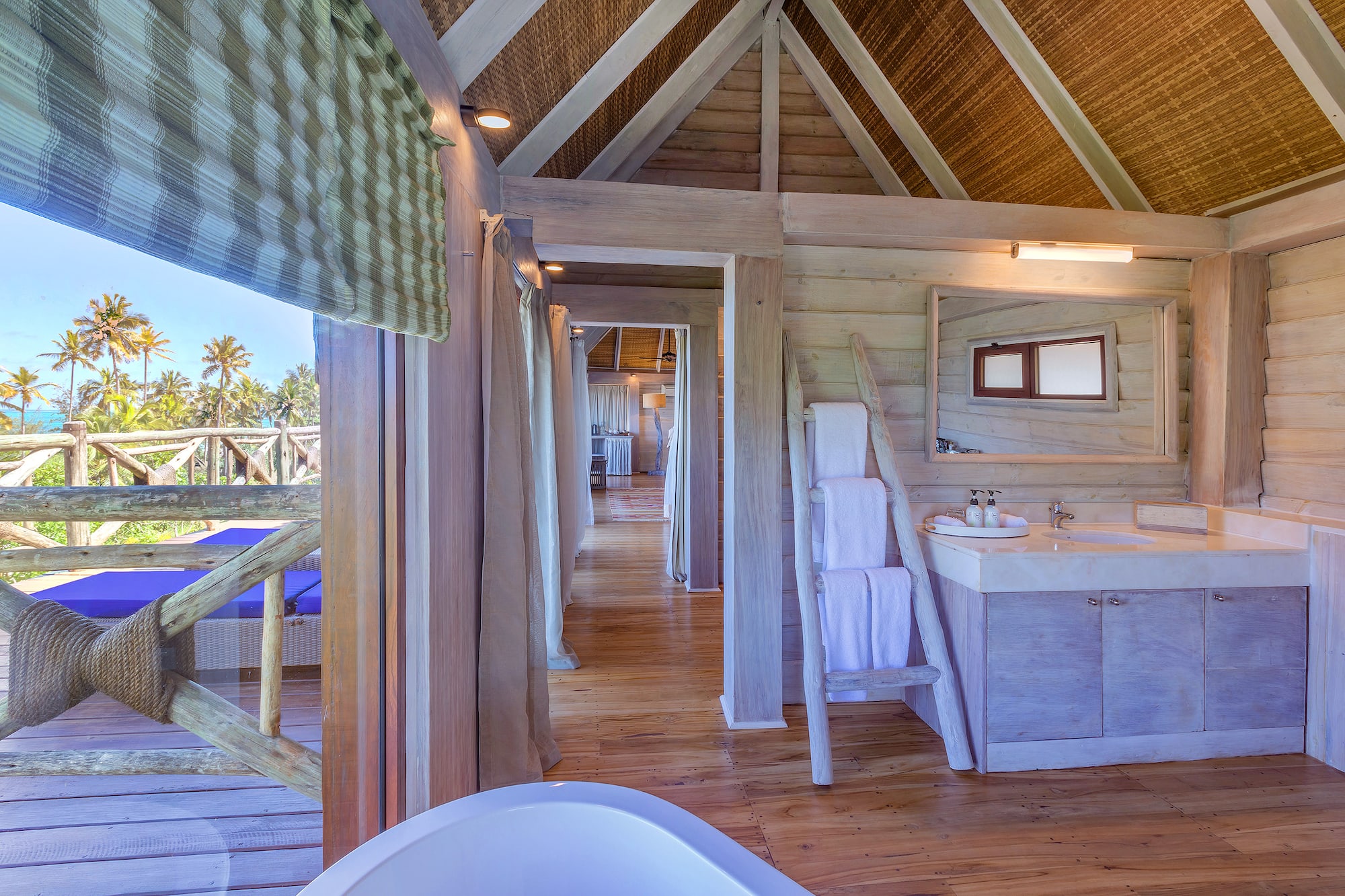 Tropical wooden bathroom in a villa with ocean view, palm trees, and vanity.