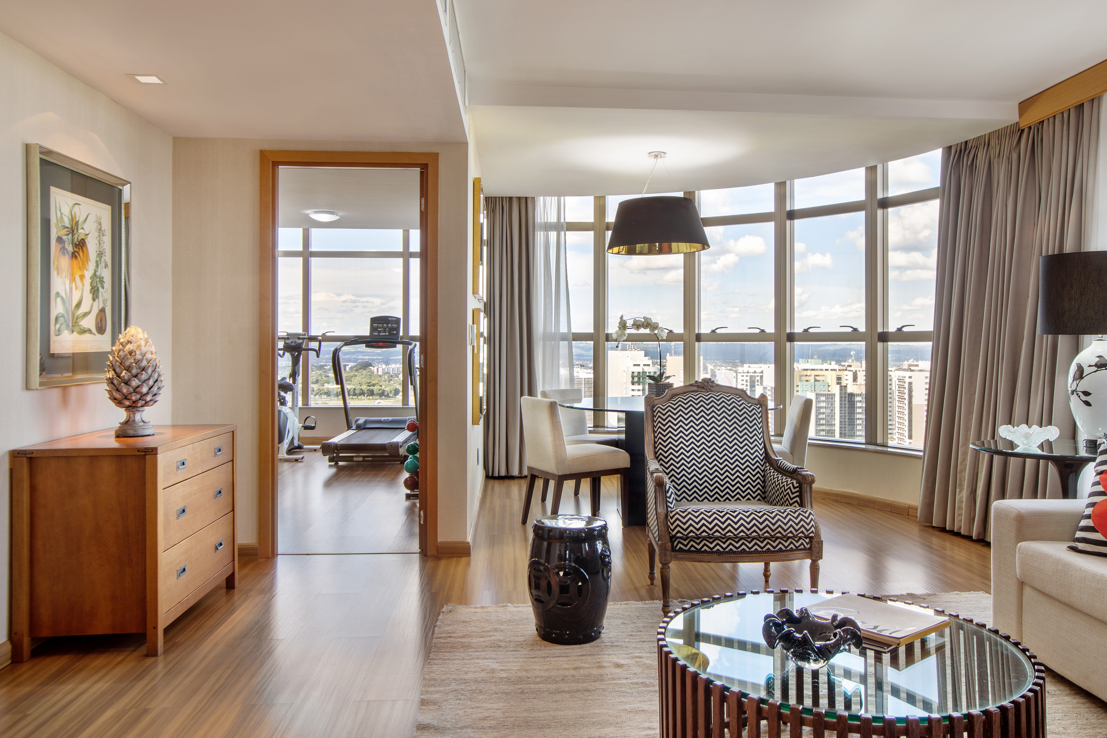 Modern apartment interior: living-dining area with city view, home gym visible.