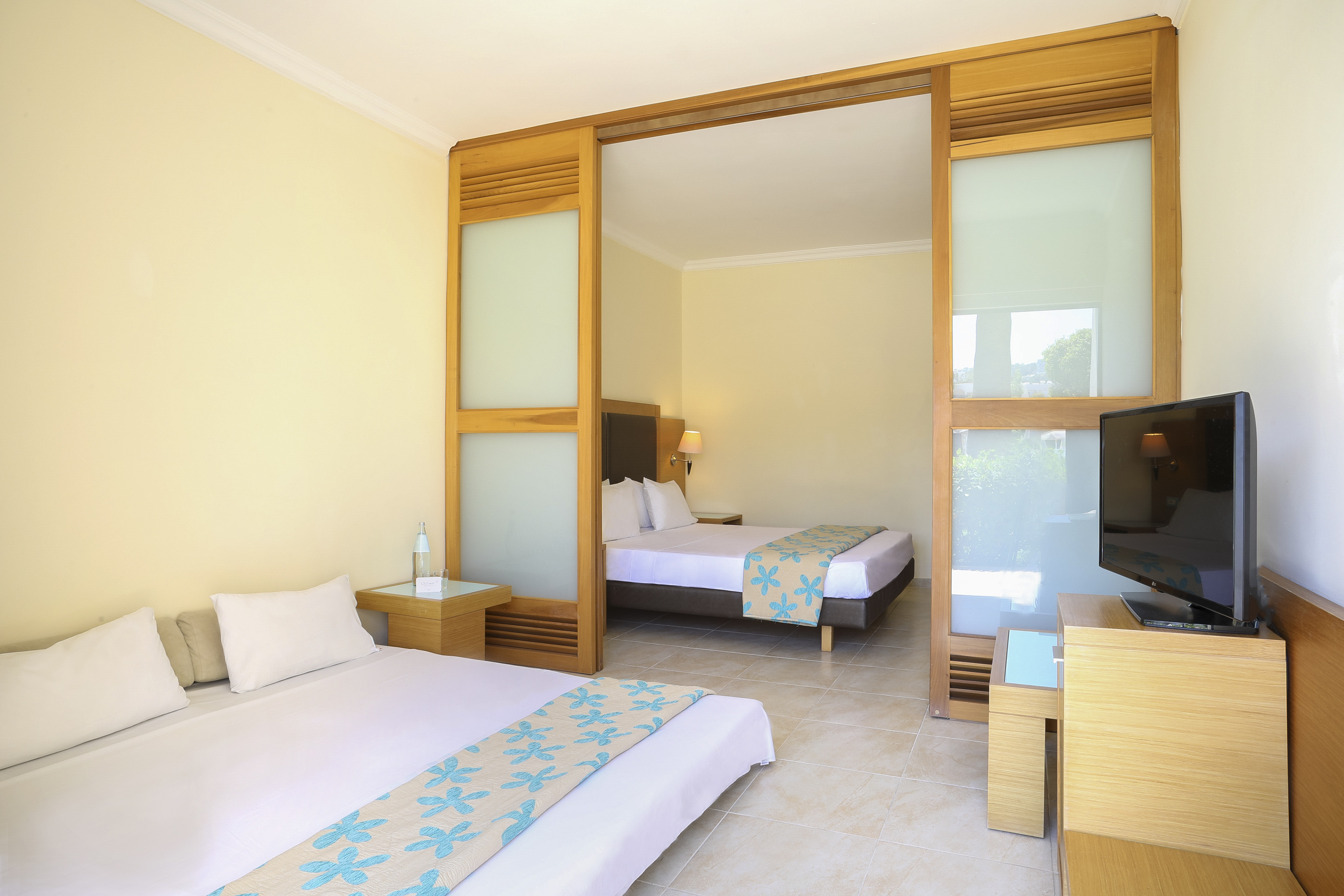 Modern hotel room with two beds, sliding room divider, and TV.