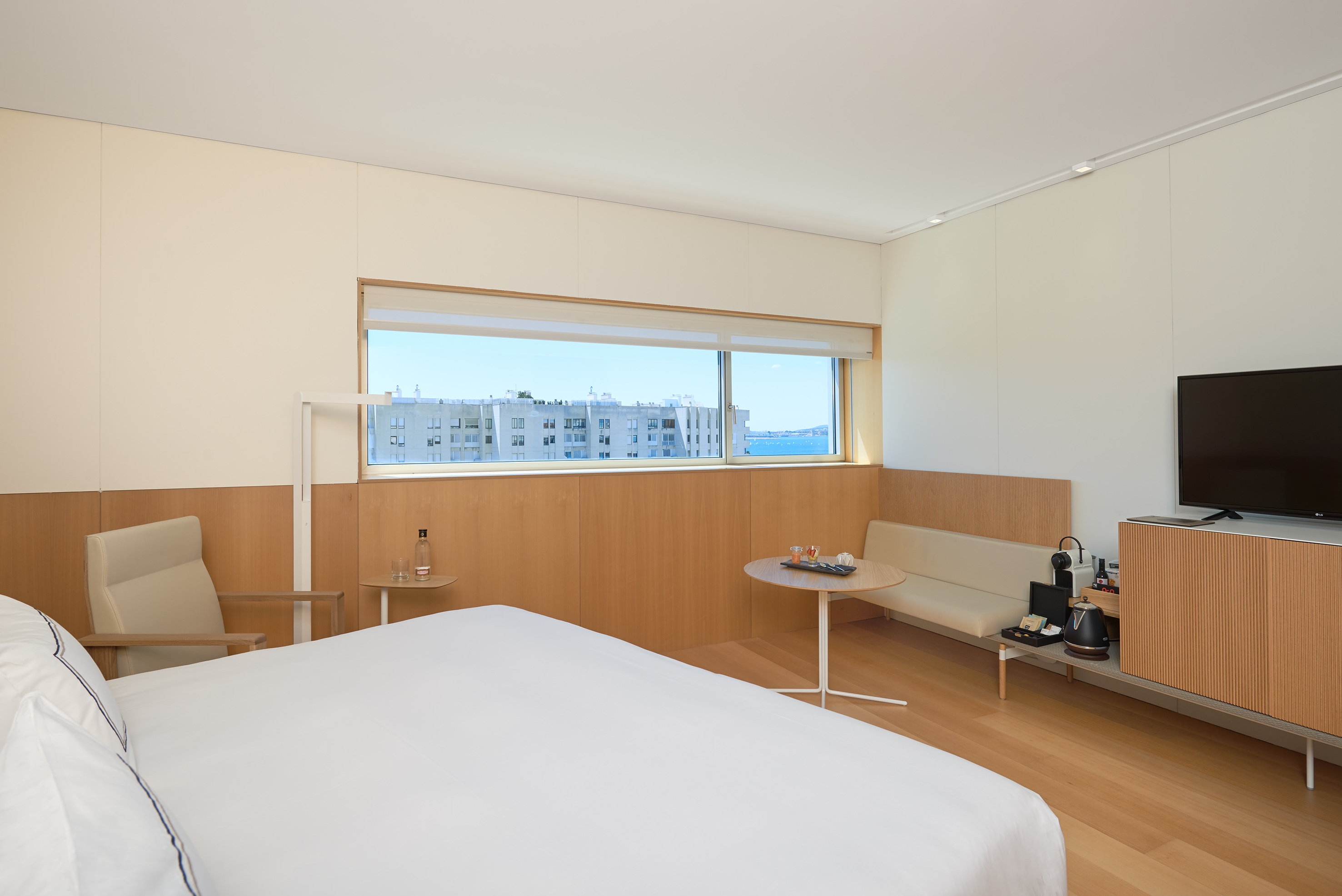 Modern hotel room with sea view, white bed, wooden floor, and sitting area.