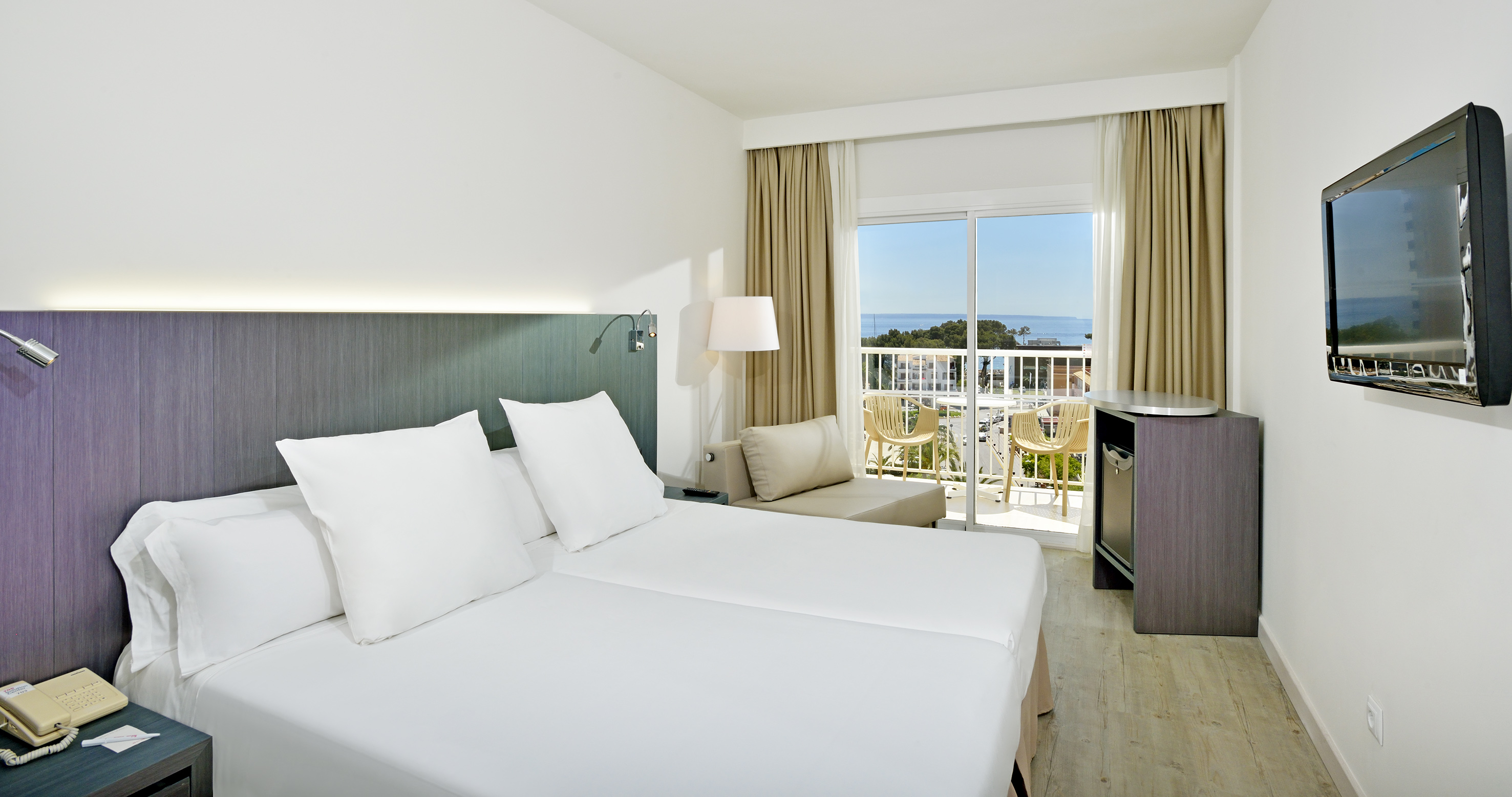 Modern hotel room with twin beds, private balcony, and ocean views.