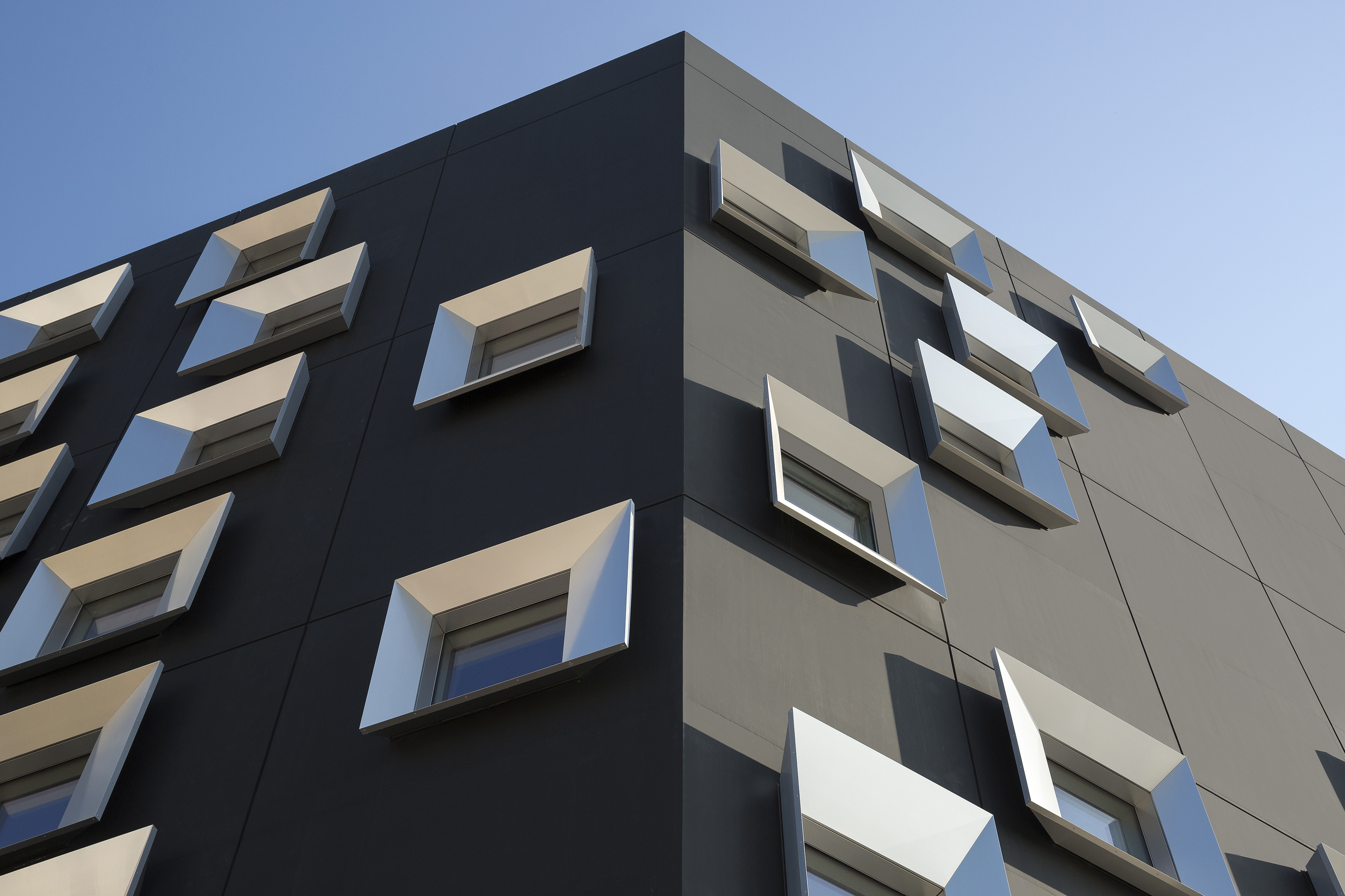 Modern dark grey building facade with unique geometric silver window frames.